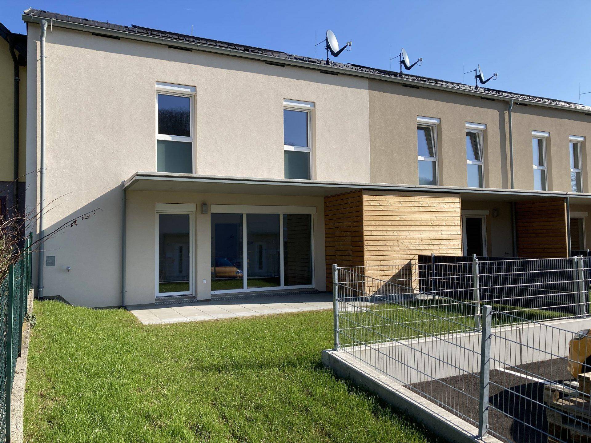 Rückseite eines Reihenhauses mit Terrasse, Rasenfläche und Blick auf die Umgebung.