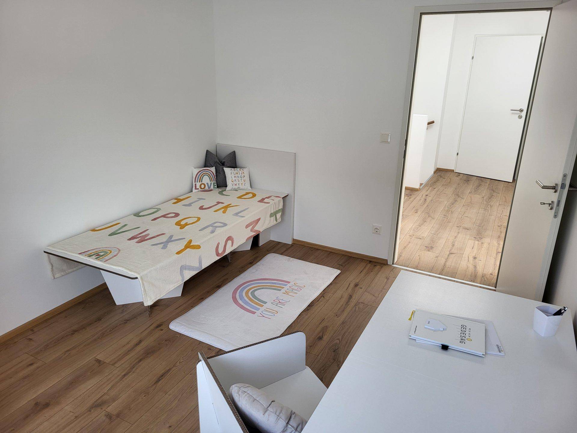 Helles Kinderzimmer mit Einzelbett, Teppich und Holzboden, ideal für junge Bewohner.