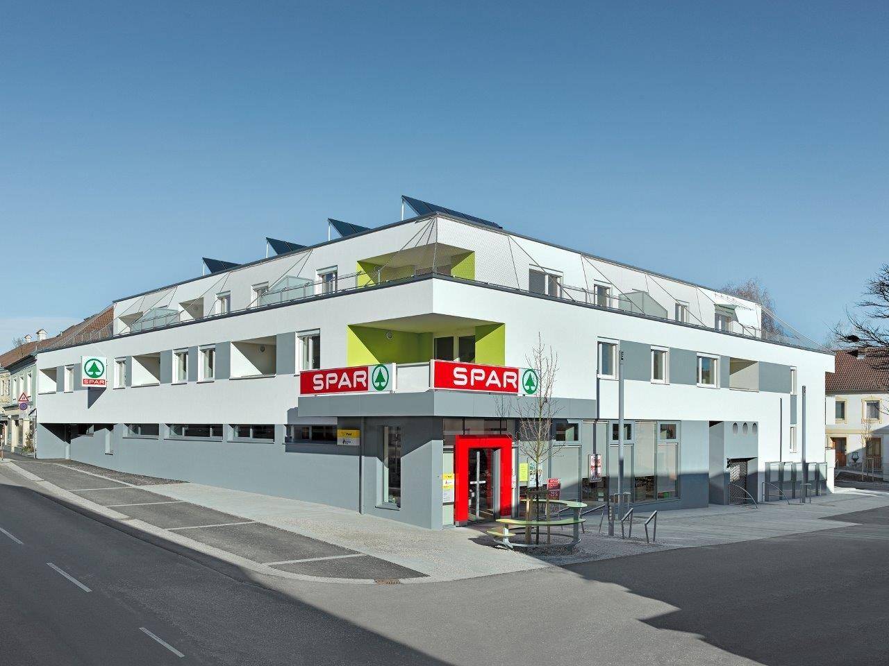 Modernes Gebäude mit integriertem Supermarkt im Erdgeschoss und Wohnungen darüber.