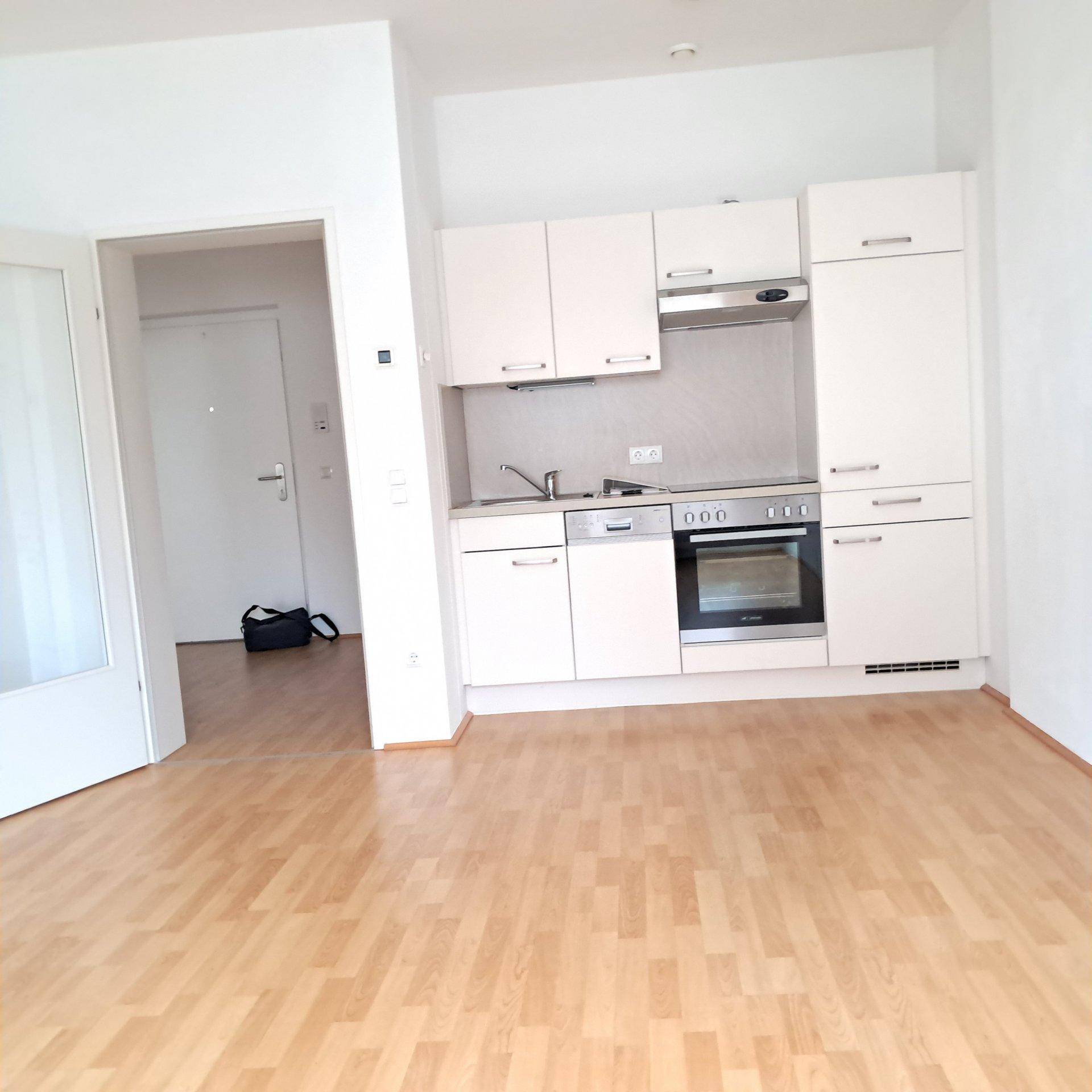 Kleine, helle Einbauküche mit weißen Schränken und Holzfußboden in offenem Raum.