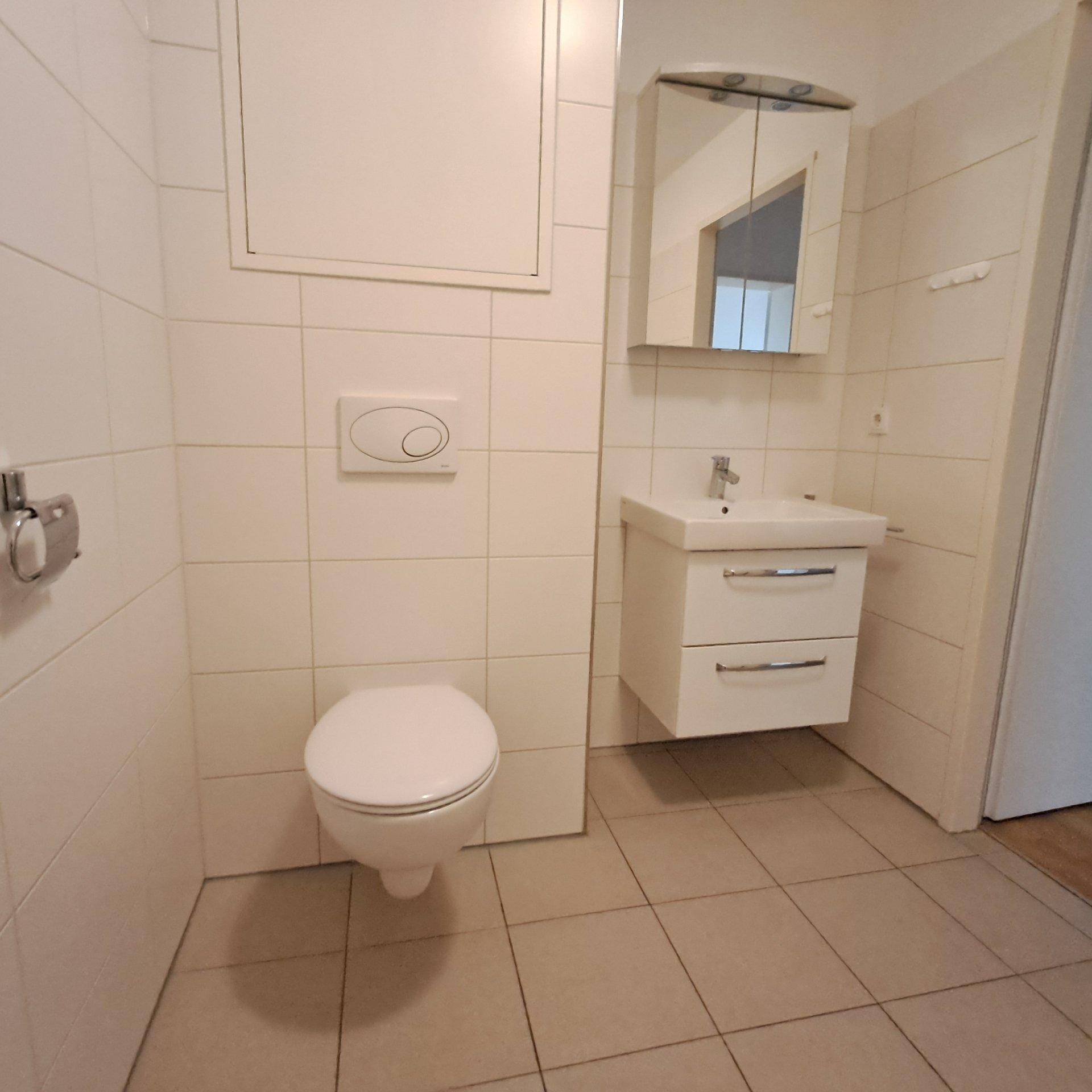 Helles Badezimmer mit weißen Fliesen, wandhängendem WC und modernem Waschtisch.