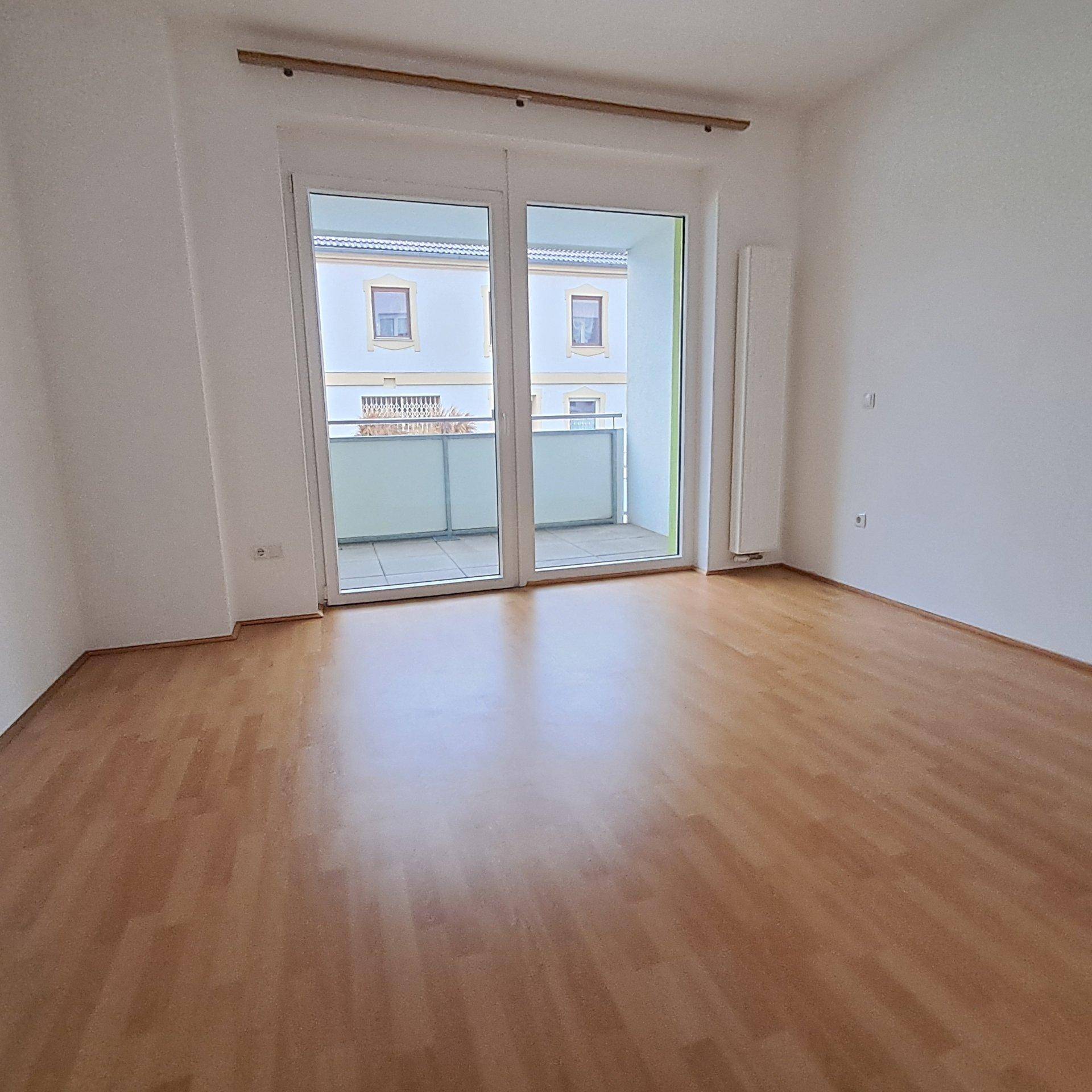 Heller Wohnraum mit Laminatboden und Zugang zu einem Balkon durch große Glastüren.