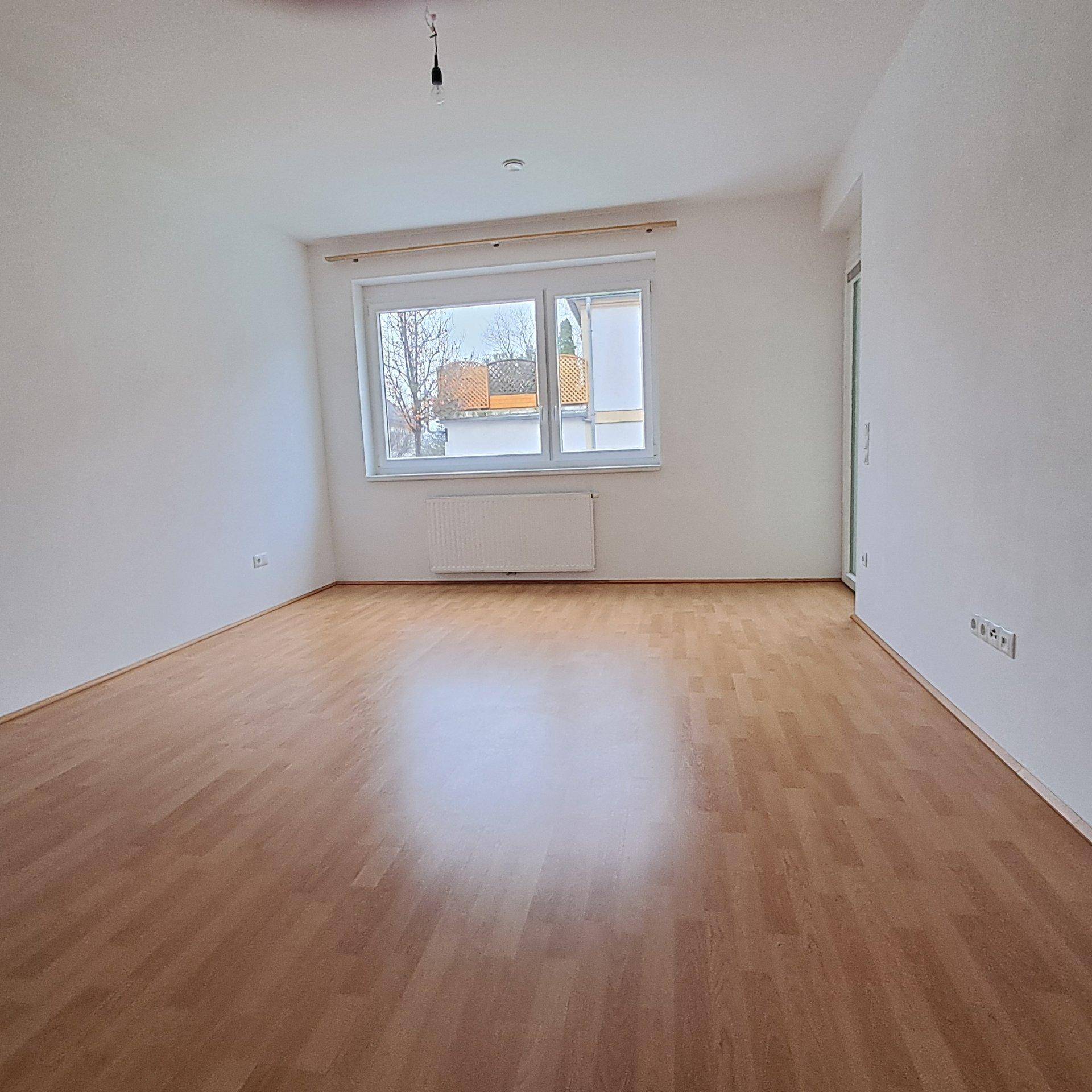 Geräumiges Zimmer mit Laminatboden und großem Fenster, das viel Tageslicht hereinlässt.