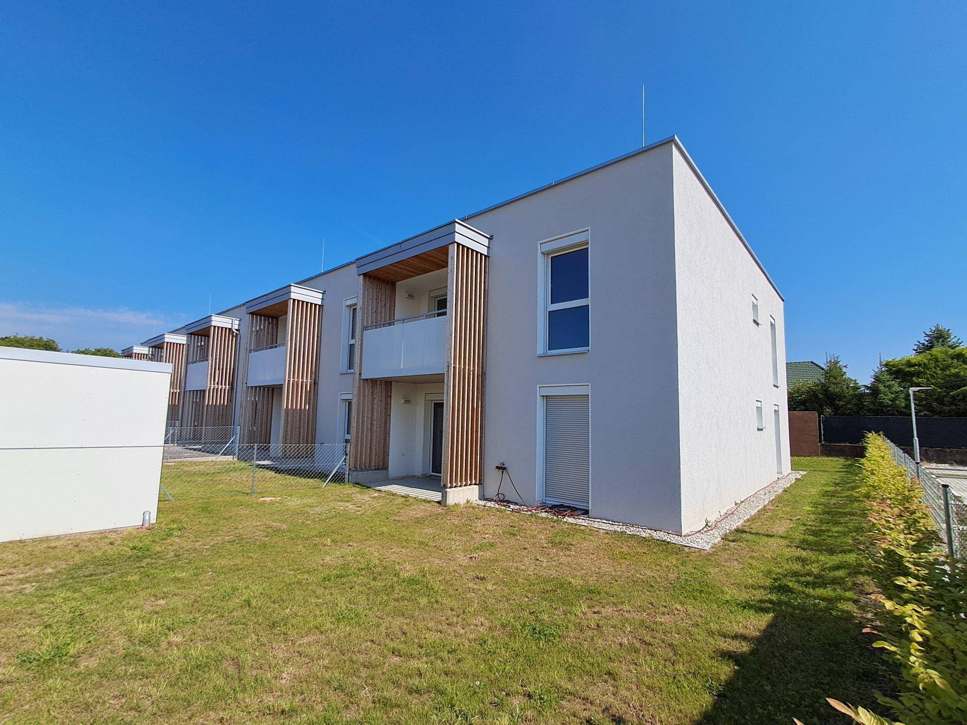 Moderne Reihenhäuser mit schlichter Fassade und großzügigen Grünflächen in sonniger Umgebung.