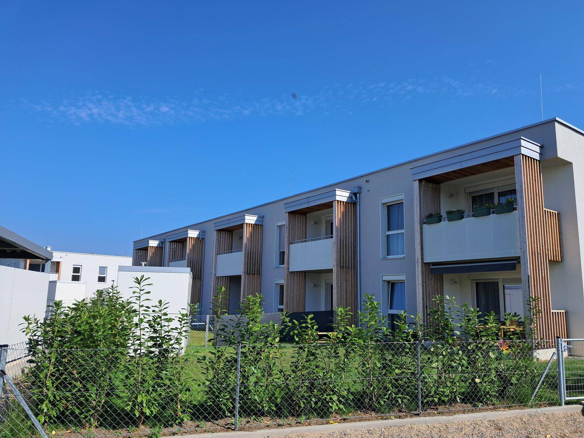 Reihenhäuser mit modernen Balkonen und Hecken als Grundstücksbegrenzung unter klarem Himmel.