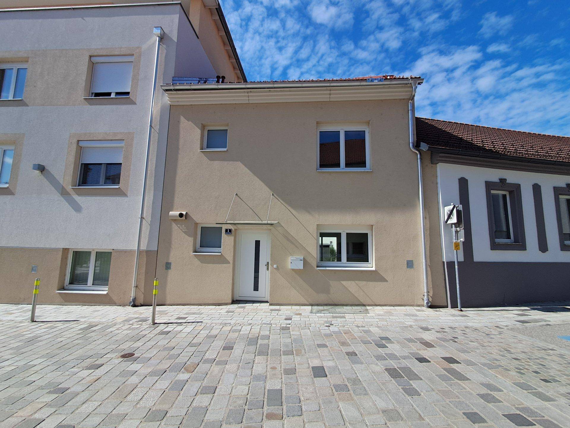 Eingangsbereich eines modernen Wohnhauses mit heller Fassade und gepflastertem Vorplatz.
