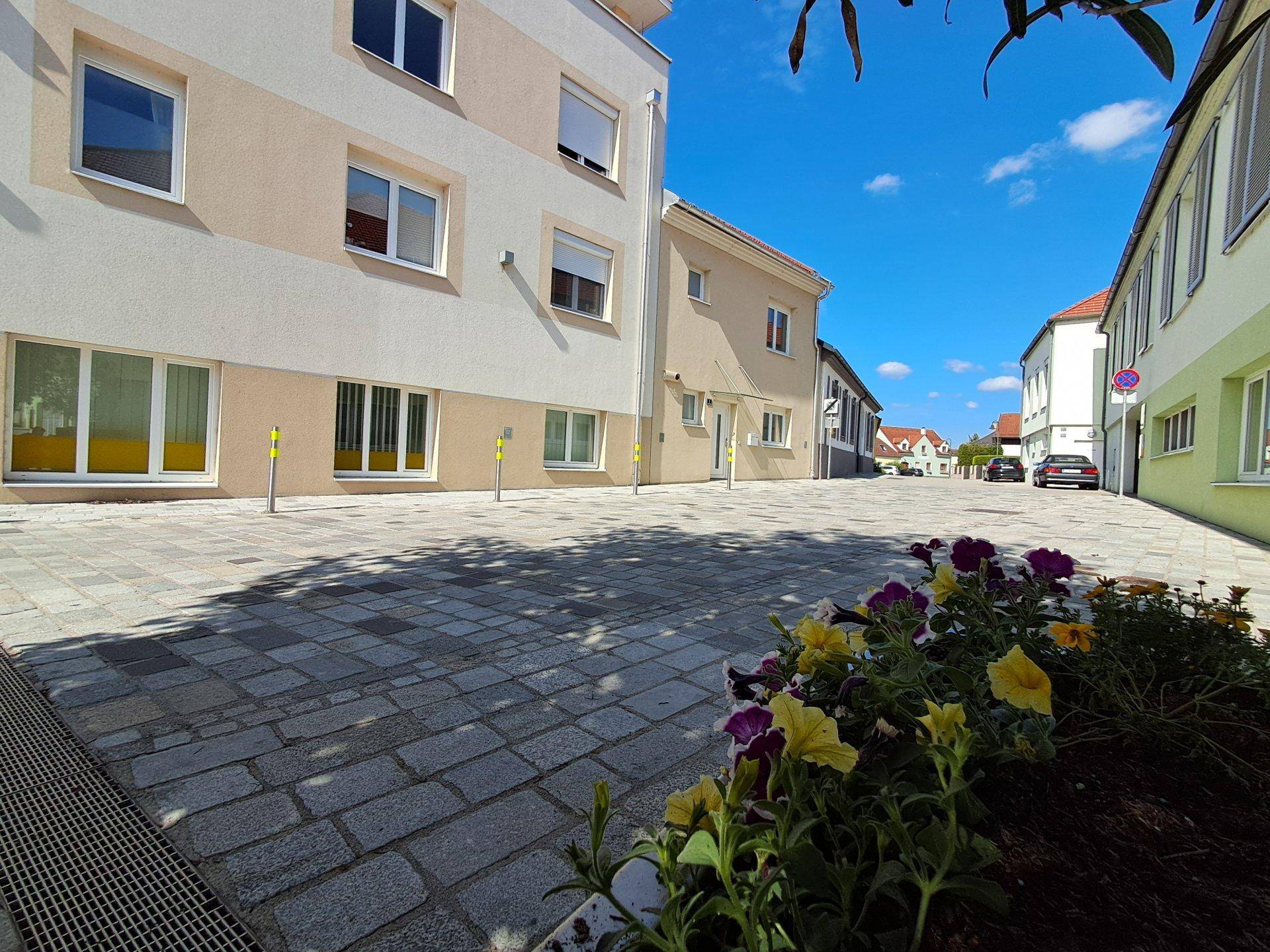 Gepflasterte Straße mit Blumenbeeten und Gebäuden in einer ruhigen Wohngegend.