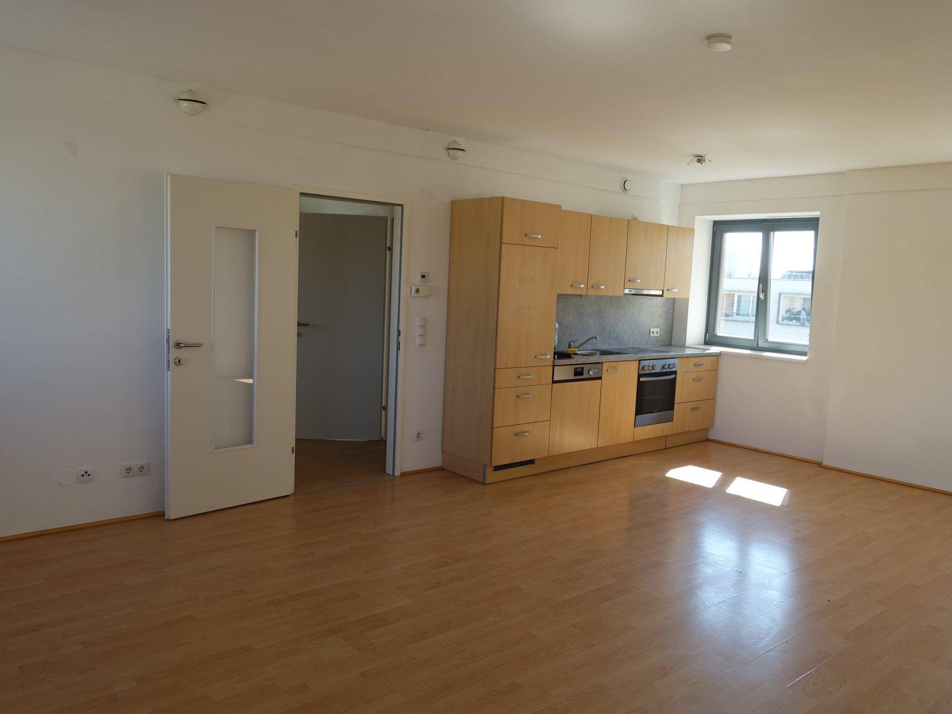 Heller Wohnbereich mit Küchenzeile, Parkettboden und viel Tageslicht durch die Fenster.