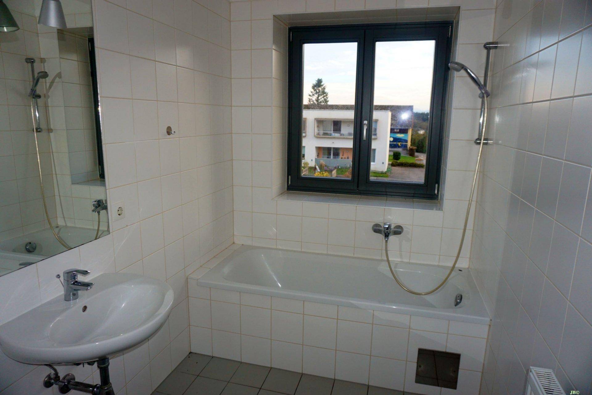 Gefliestes Badezimmer mit Badewanne, Duschfunktion, Waschbecken und Fenster für Belüftung.