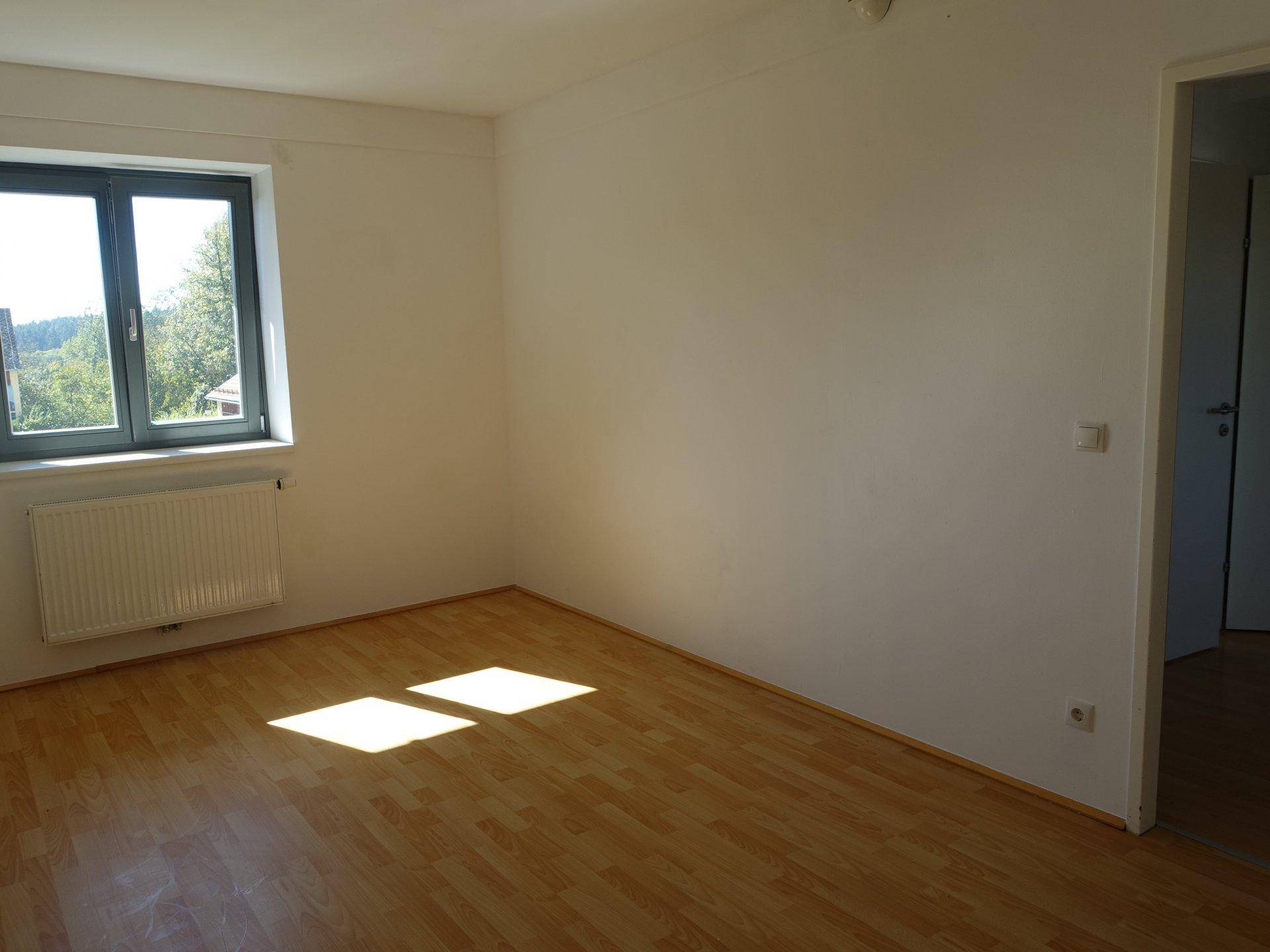 Helles Zimmer mit Parkettboden und Fenster, das viel Sonnenlicht hereinlässt und Blick ins Grüne bietet.