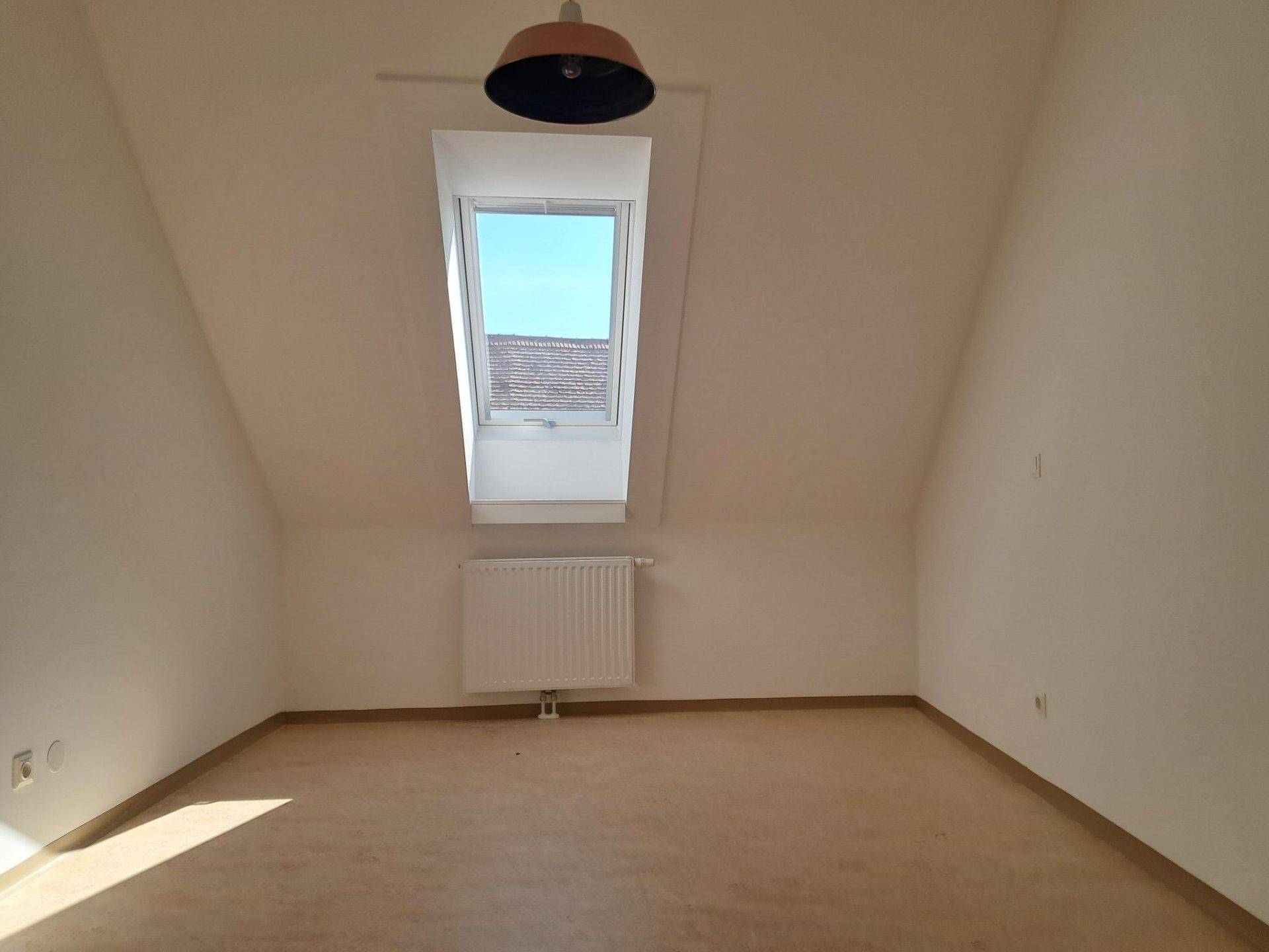 Lichtdurchfluteter Dachgeschossraum mit einem großen Dachfenster und Heizkörper.