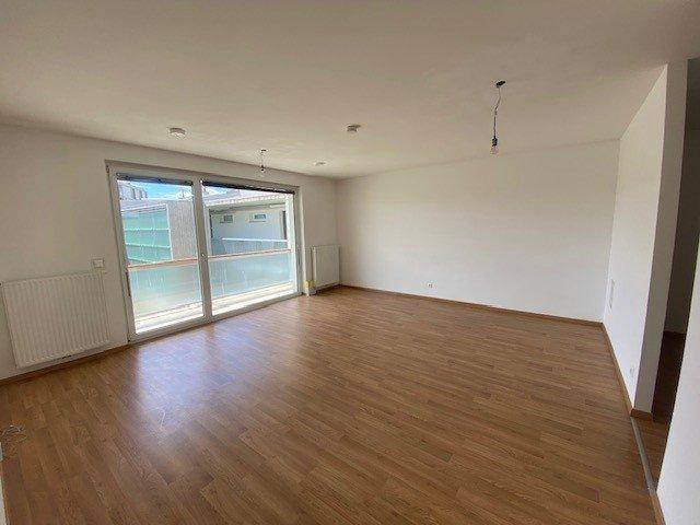 Helles, leeres Wohnzimmer mit Parkettboden und großem Fenster mit Balkonzugang.
