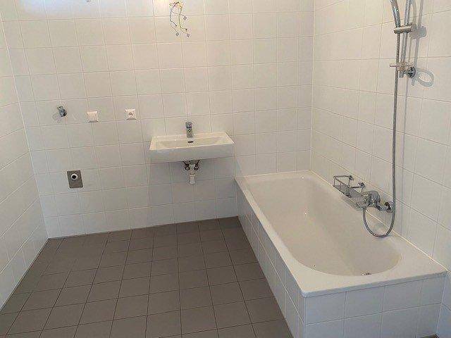 Funktionales Badezimmer mit Badewanne, Waschbecken und weißen Fliesen an Wänden und Boden.