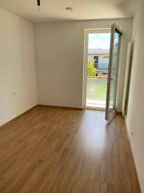 Leeres Schlafzimmer mit Holzboden und Zugang zum Außenbereich durch eine Balkontür.