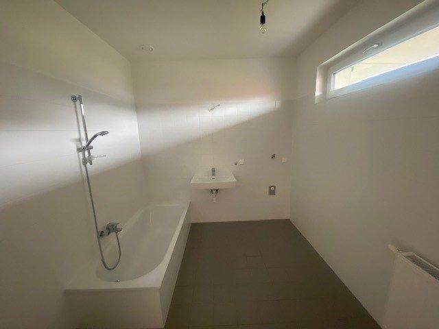 Modernes Badezimmer mit Badewanne, Waschbecken und einem schmalen Fenster.