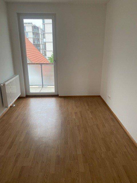 Helles Schlafzimmer mit Laminatboden und Tür zu einem Balkon oder einer Terrasse.