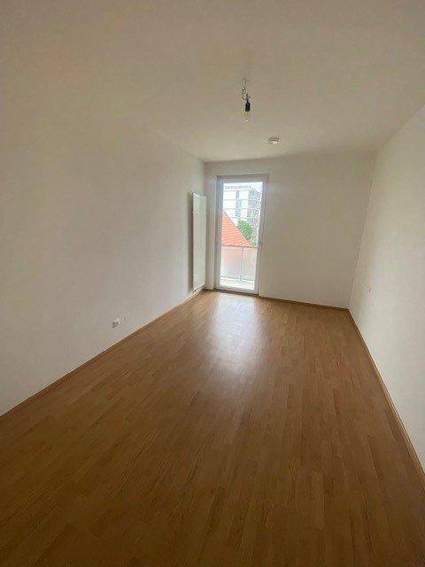 Leeres Schlafzimmer mit Laminatboden und Zugang zu einem kleinen Außenbereich.