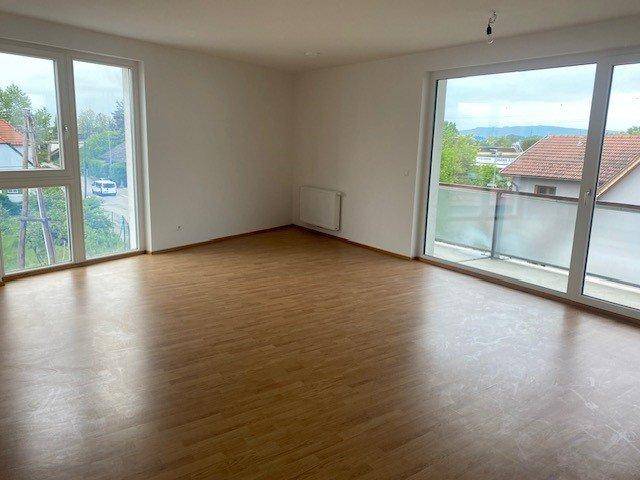 Helles Wohnzimmer mit großen Fenstern, Laminatboden und Zugang zu einem Balkon.