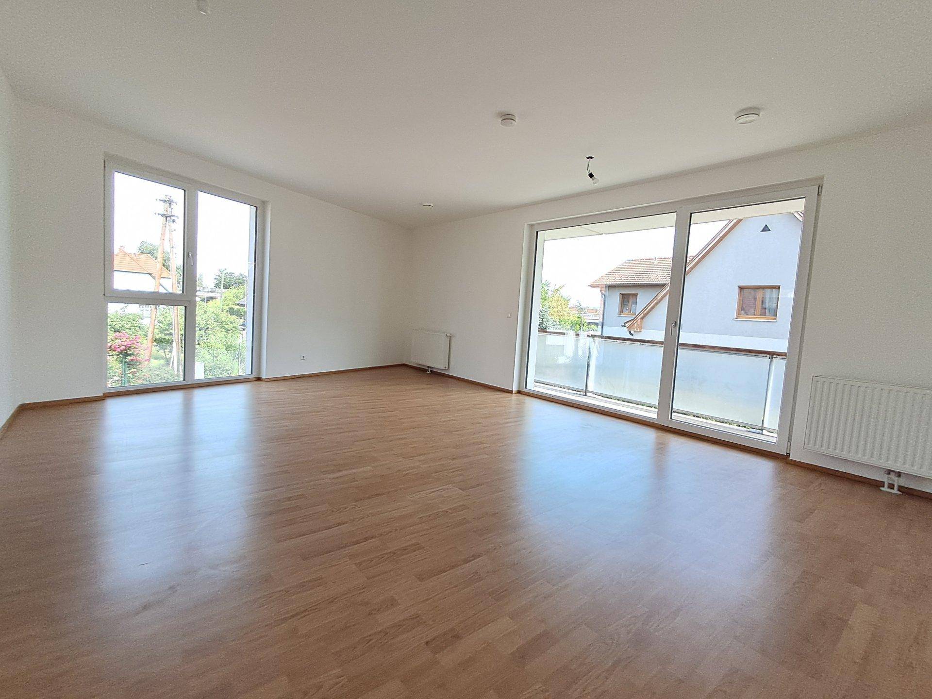 Helles Wohnzimmer mit großen Fenstern, Laminatboden und Zugang zum Balkon.