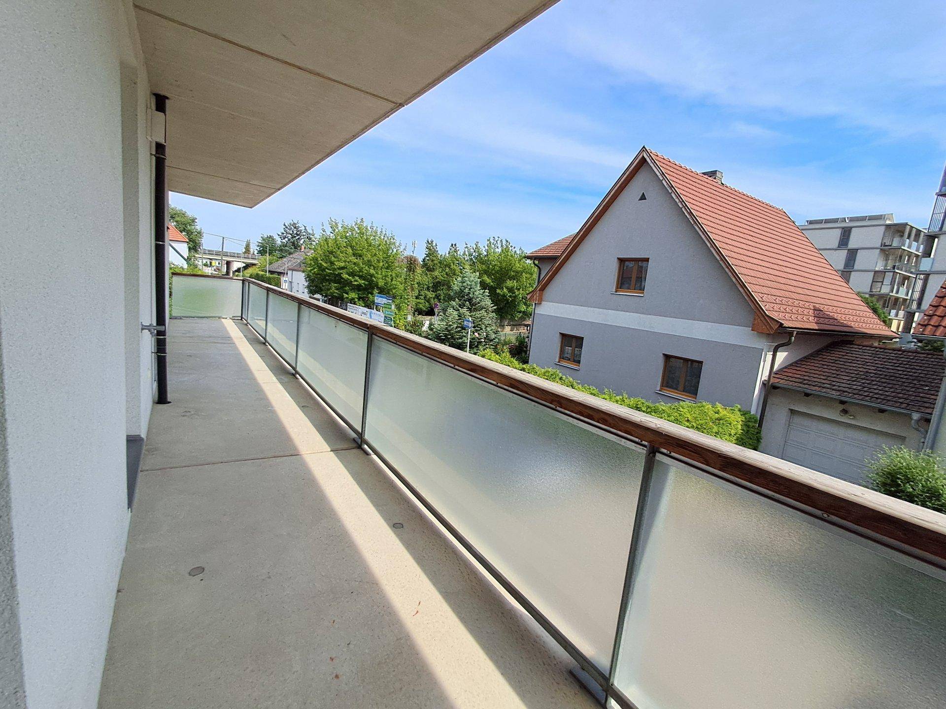 Langer, leerer Balkon mit Milchglasgeländer und Blick auf die Umgebung.