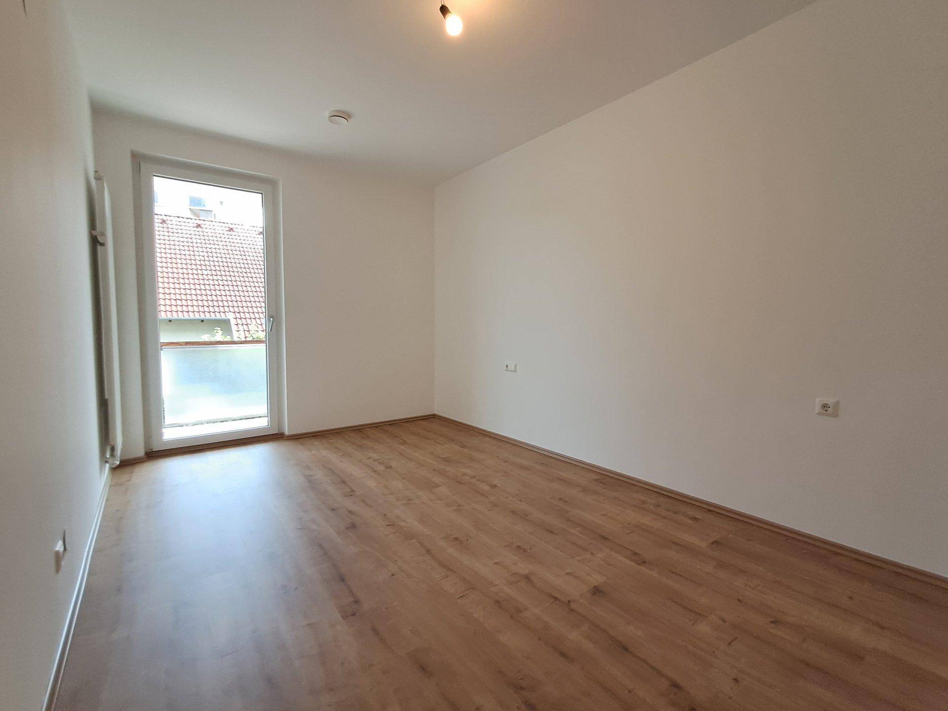 Schlafzimmer mit Laminatboden, weiß gestrichenen Wänden und Balkonzugang.