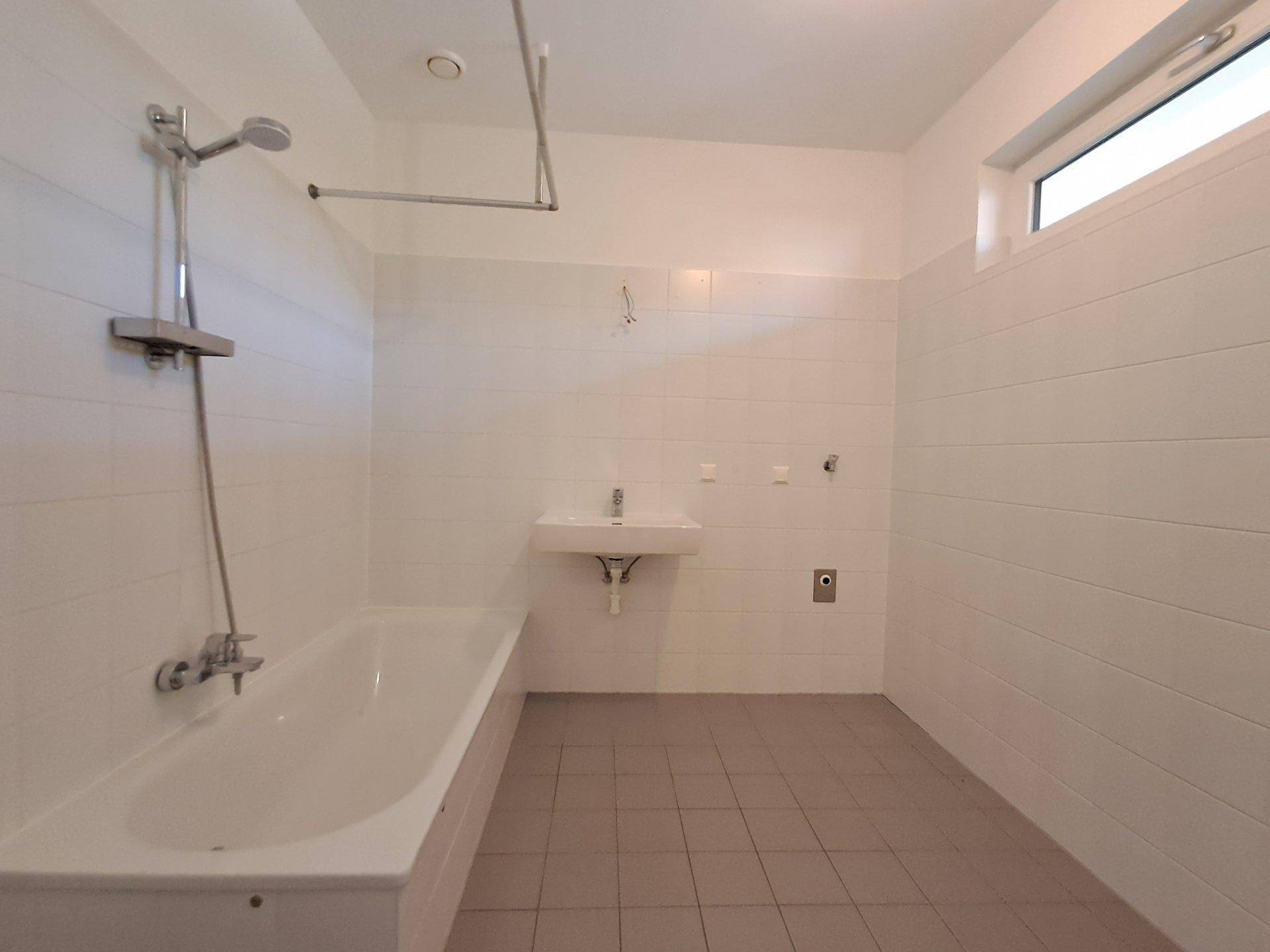 Helles Badezimmer mit Badewanne, Fliesenboden und Fenster.