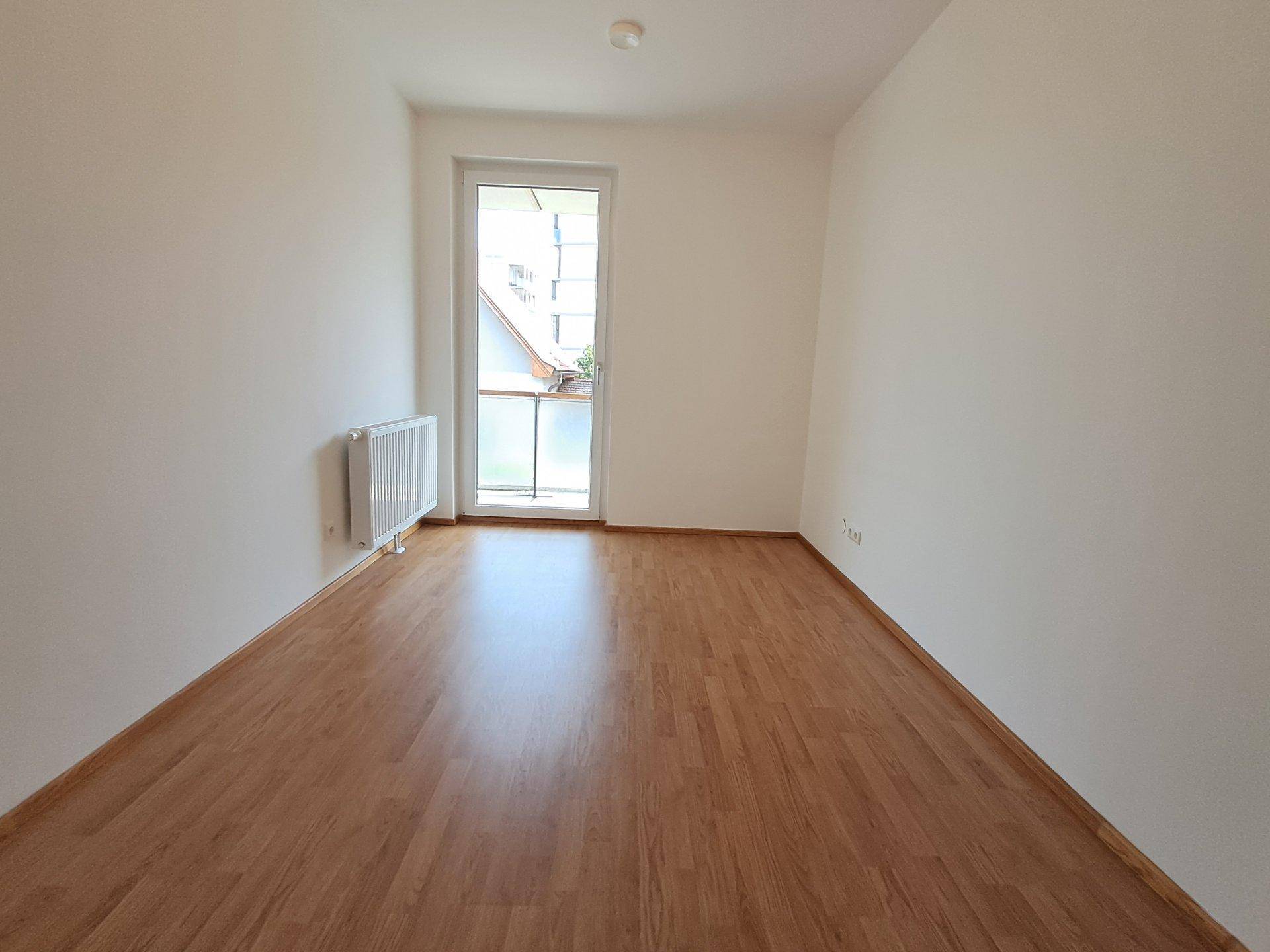Geräumiges Schlafzimmer mit Laminatboden und großem Fenster.