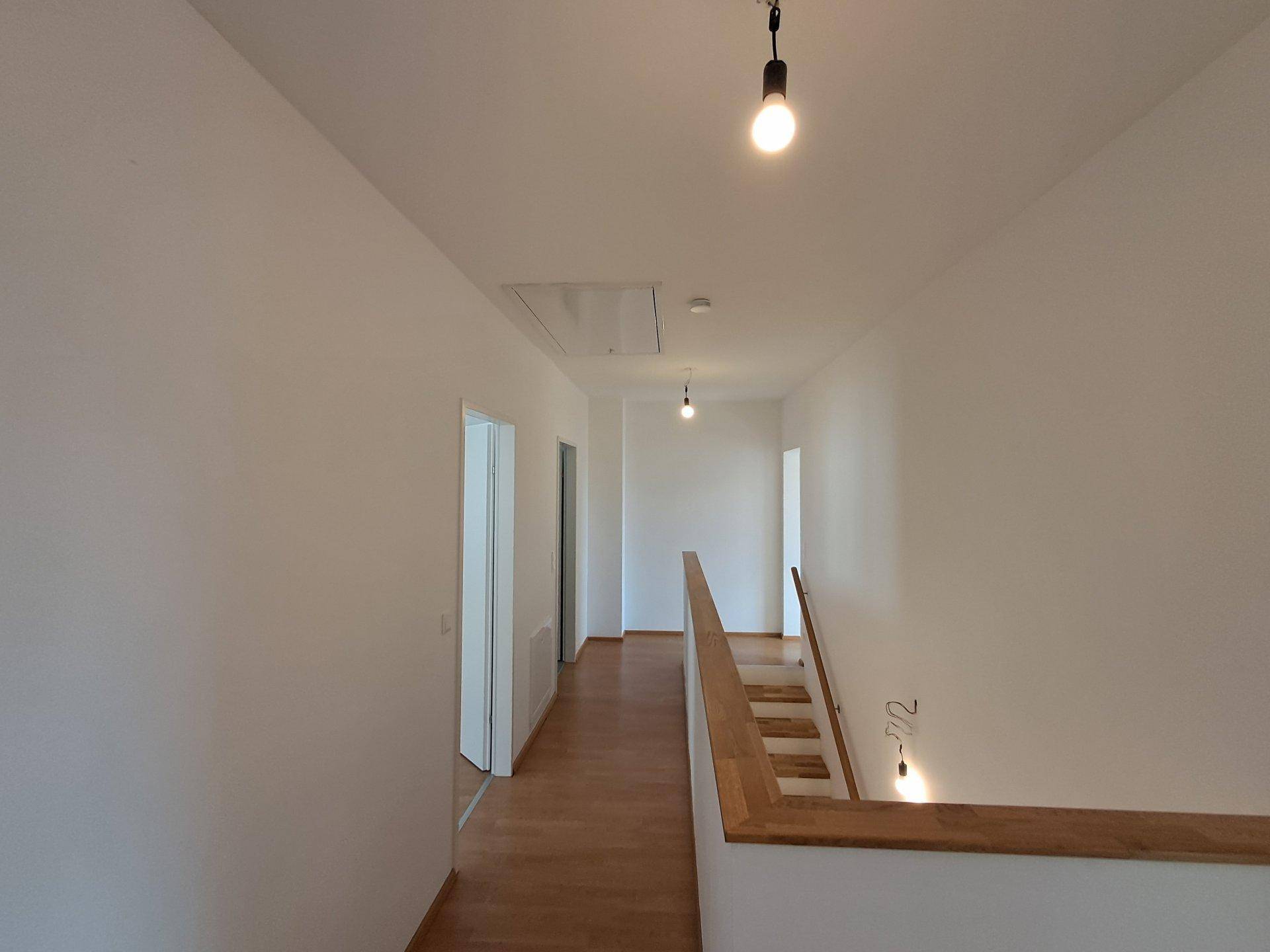Heller Flur im Obergeschoss mit Laminatboden und Zugang zu weiteren Zimmern, gut beleuchtet.