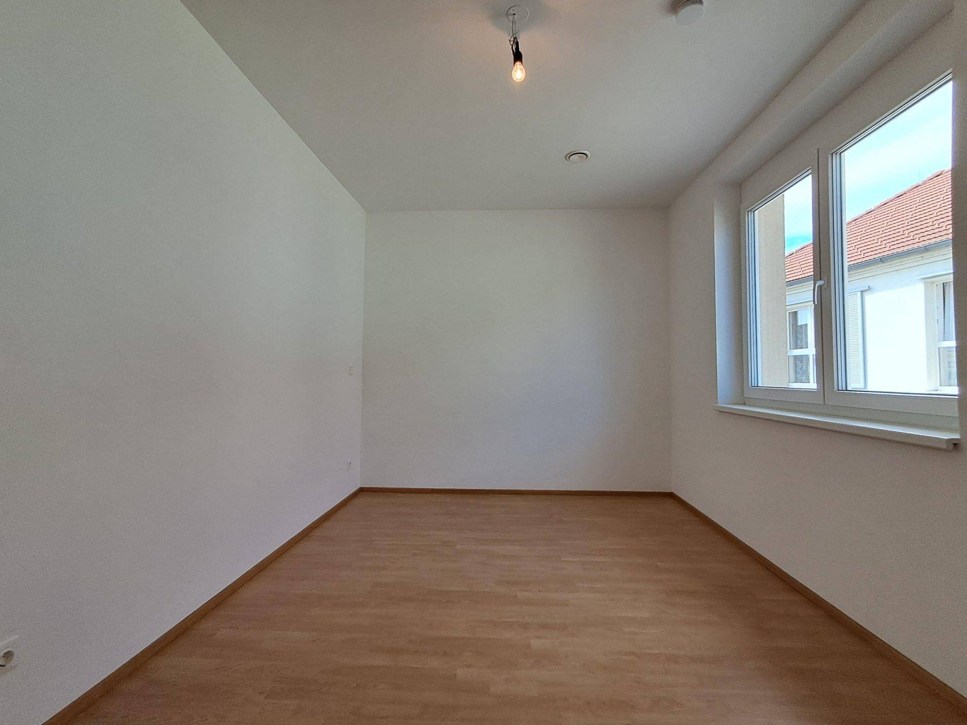 Geräumiges Schlafzimmer mit Laminatboden und Fenster, das eine angenehme Helligkeit bietet.