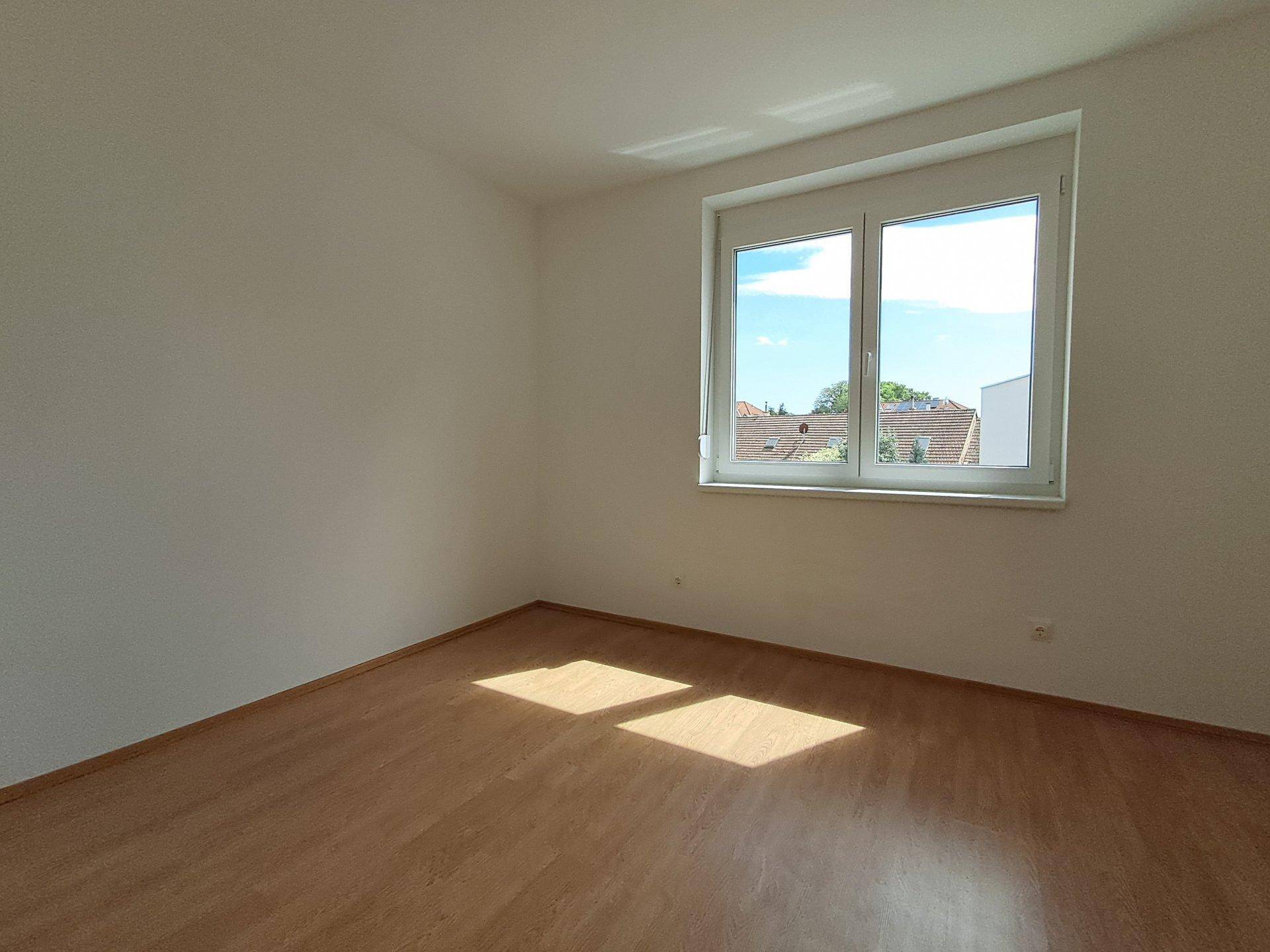 Lichtdurchflutetes Schlafzimmer mit Laminatboden und Blick auf die umliegenden Dächer.