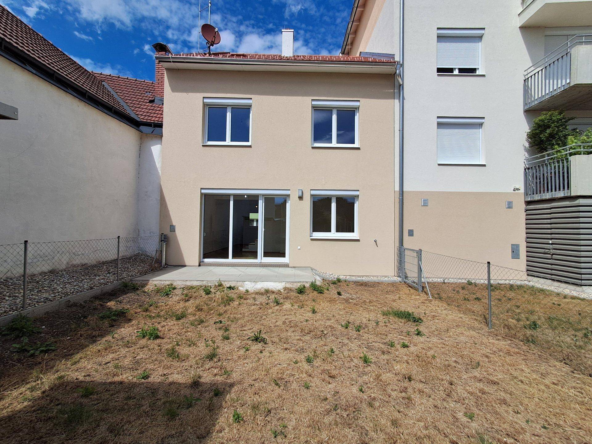 Hinterer Gartenbereich mit Rasenfläche und der Rückseite des Hauses mit Terrassenzugang.
