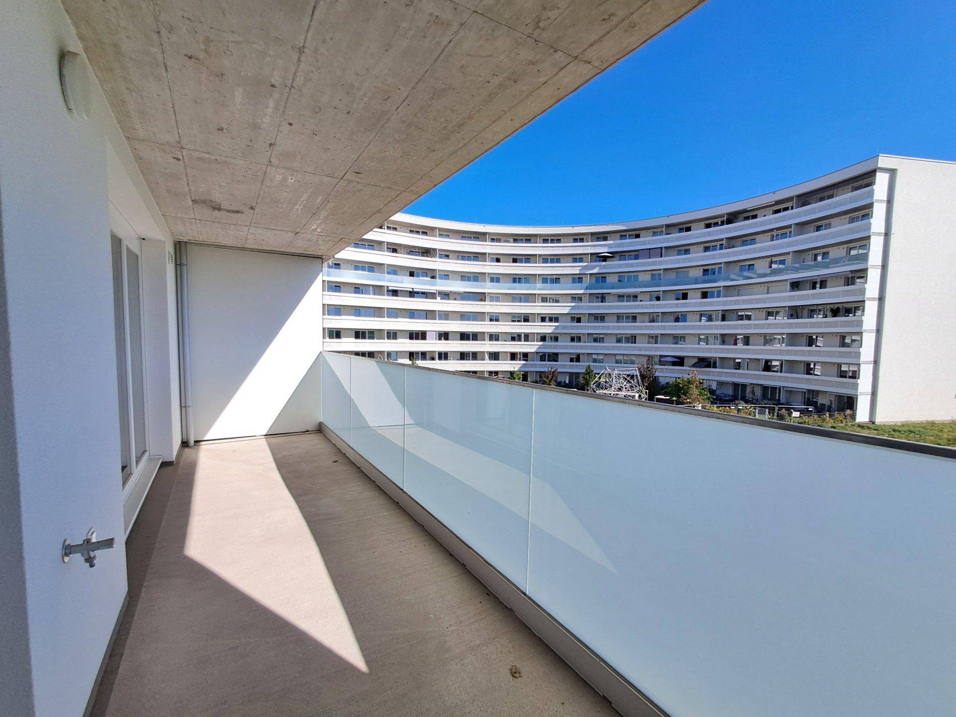 Geräumiger Balkon mit moderner Glasbrüstung und Blick auf ein weiteres Wohngebäude in der Nachbarschaft.