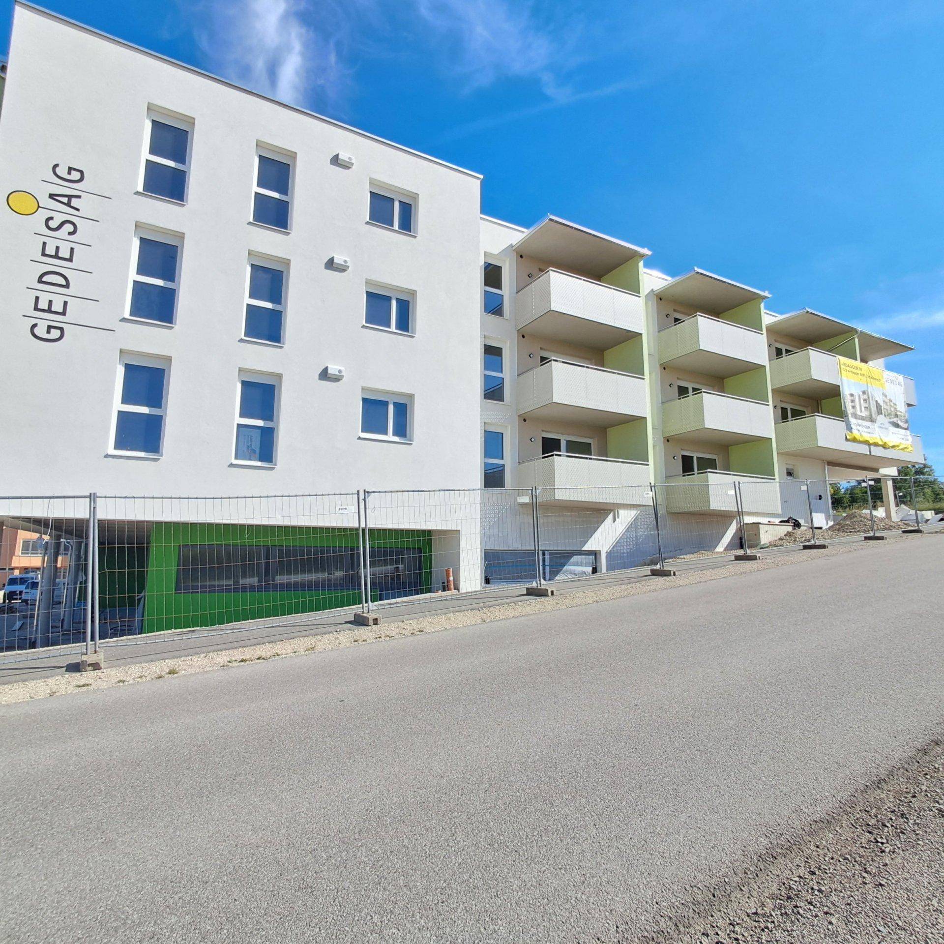 Modernes Neubau-Wohngebäude mit weißen Wänden, grünen Akzenten und Balkonen unter klarem Himmel.