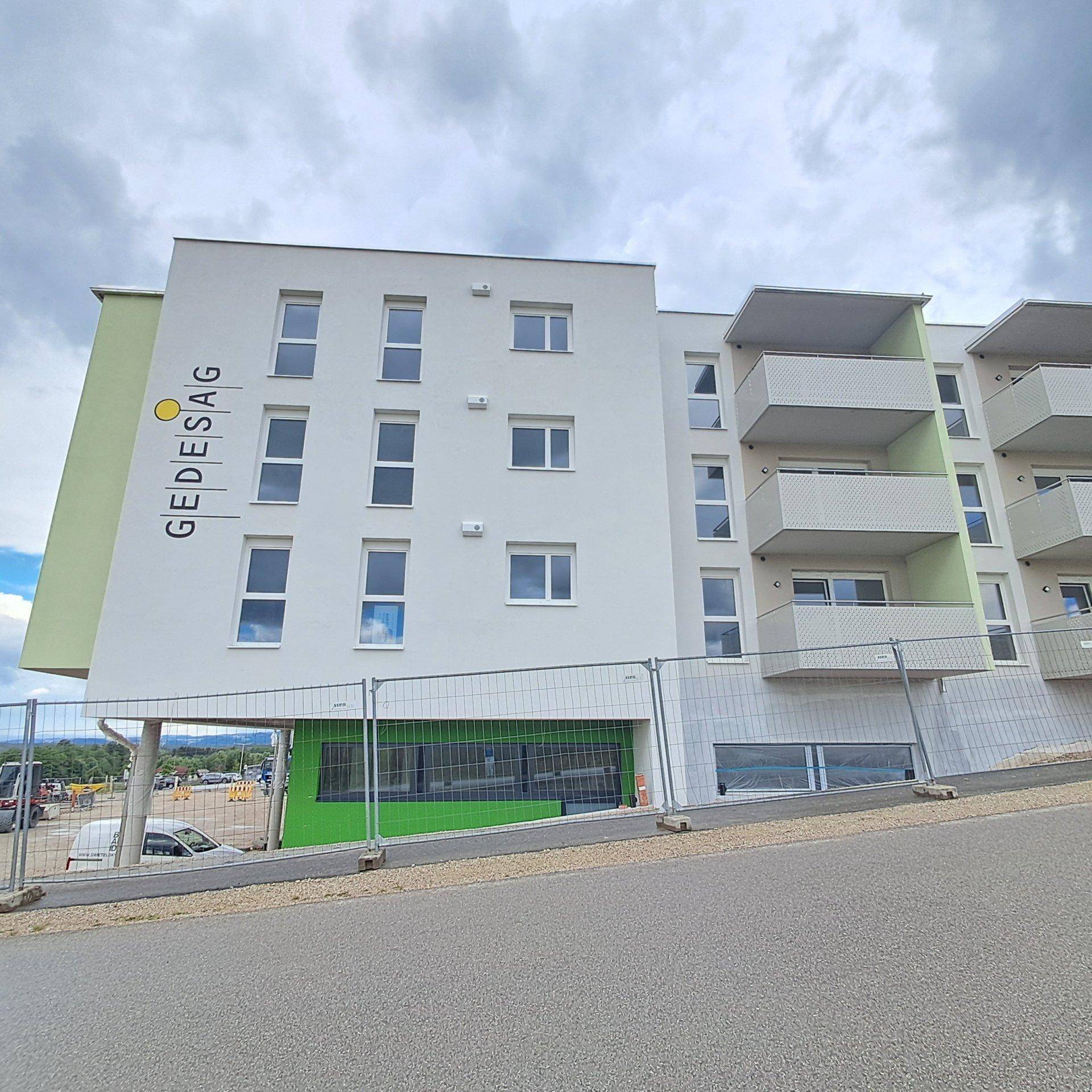 Neubau-Wohngebäude mit weißen Fassaden, grünen Elementen und Balkonen an einem bewölkten Tag.