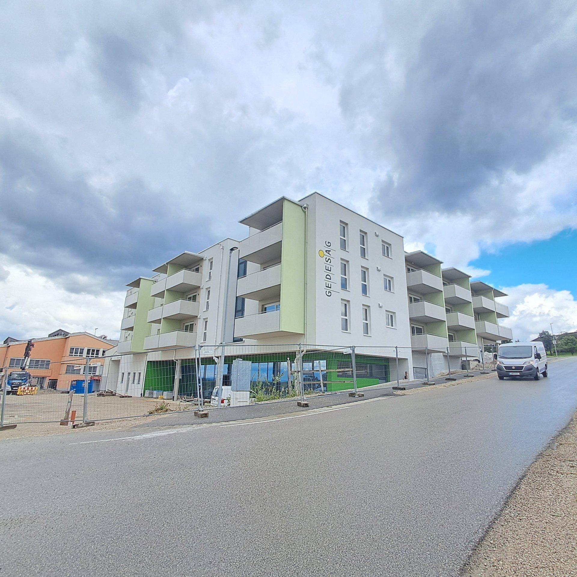 Neubau-Wohnkomplex mit Balkonen und grünen Fassadenelementen an einem bewölkten Tag.