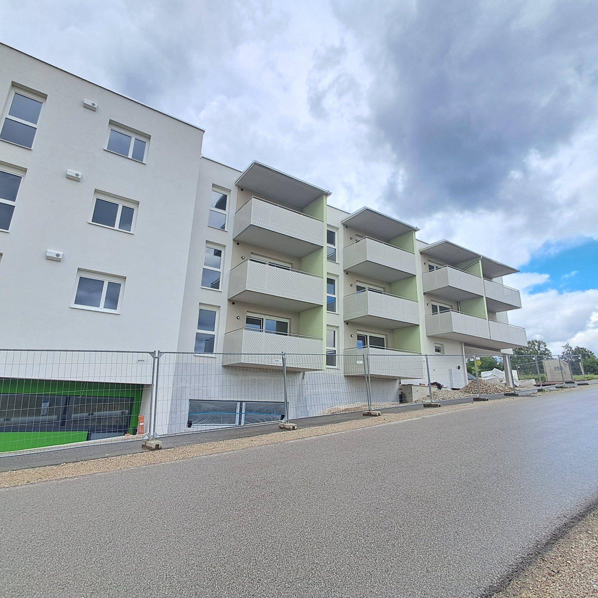 Modernes Neubau-Wohngebäude mit weißen Fassaden, grünen Akzenten und Balkonen an einem bewölkten Tag.