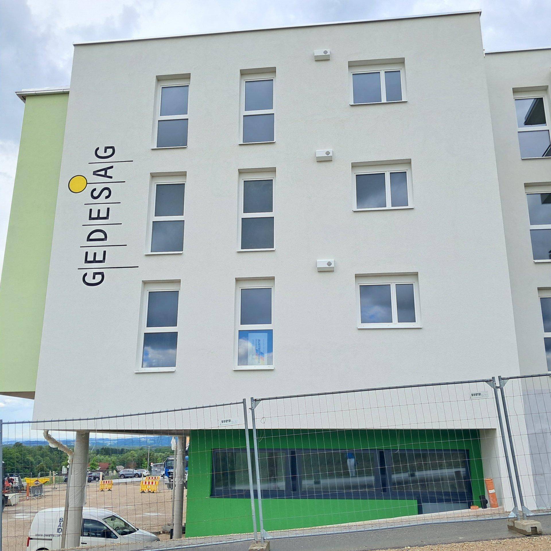 Detailansicht der weißen Fassade eines Neubaus mit grünen Akzenten und Fenstern.