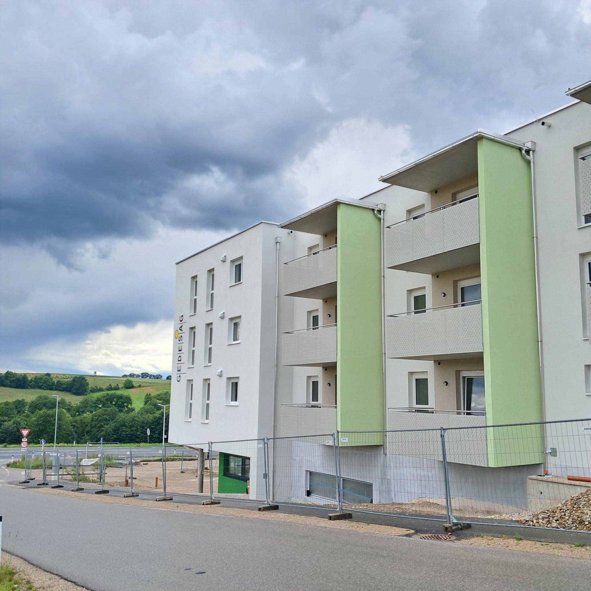 Modernes Wohngebäude mit Balkonen und Blick auf die umliegende grüne Landschaft.
