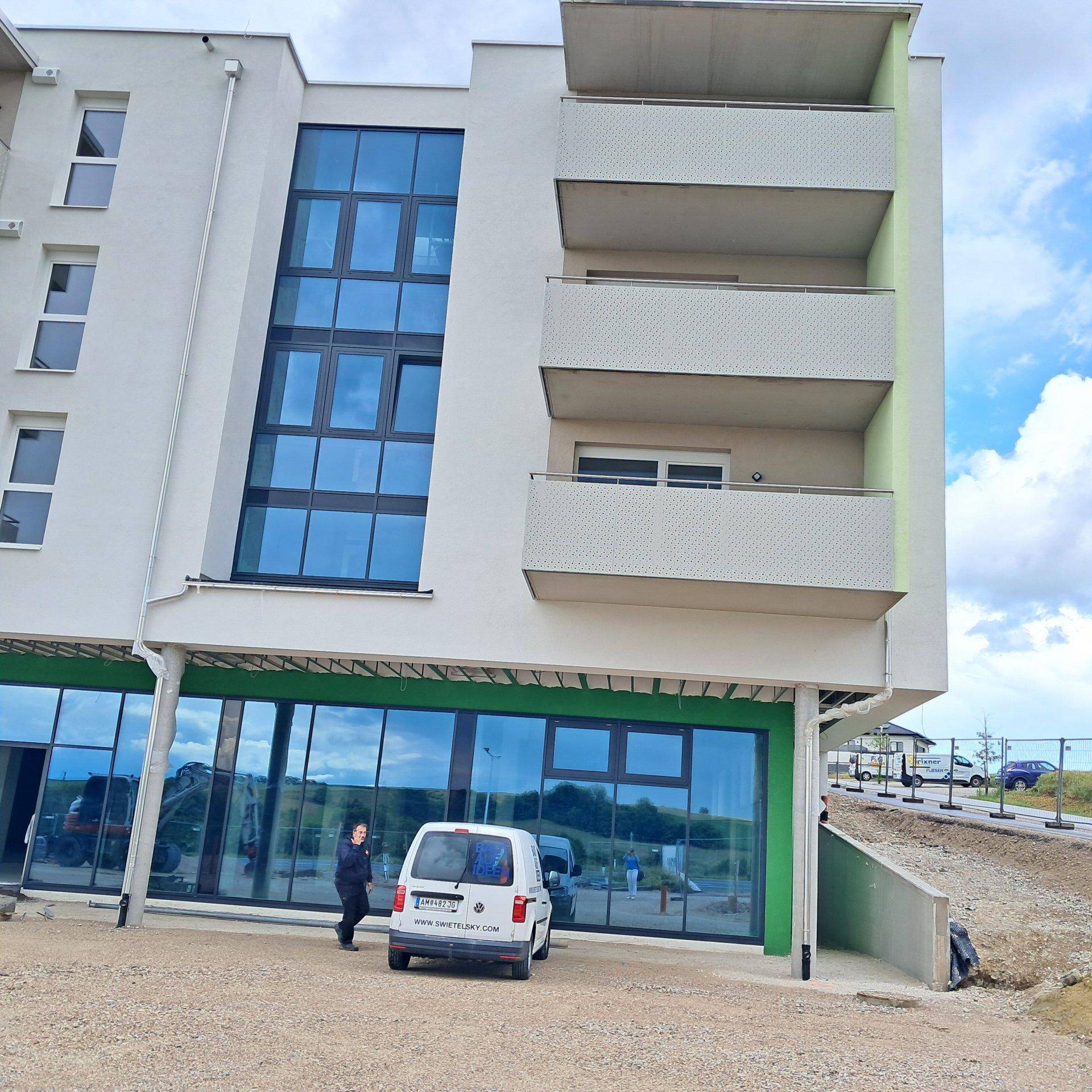 Modernes Gebäude mit großen Glasfronten im Erdgeschoss und Balkonen in der oberen Etage.