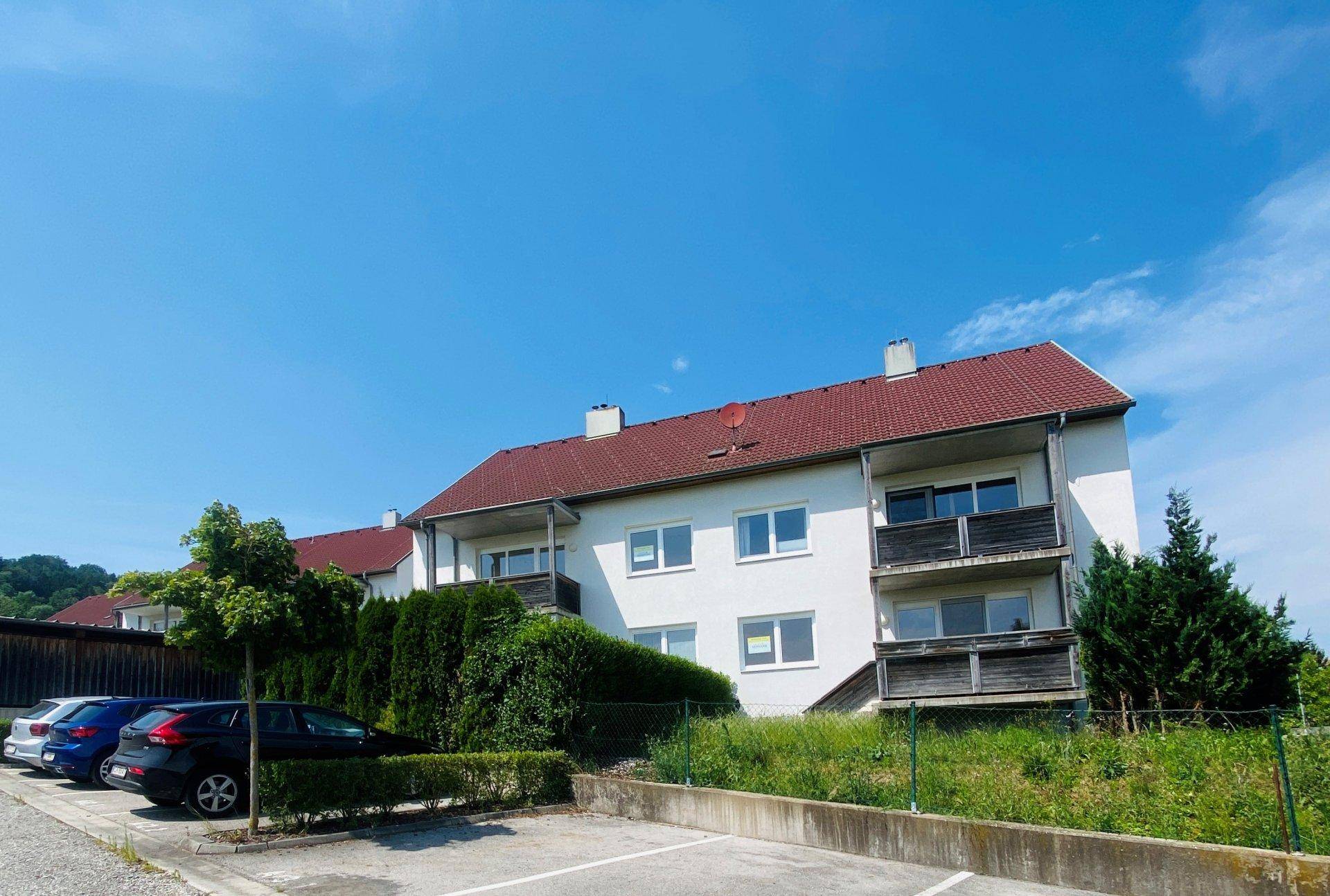 Mehrere Wohnhäuser mit roten Dächern und einem Parkplatz im Vordergrund.