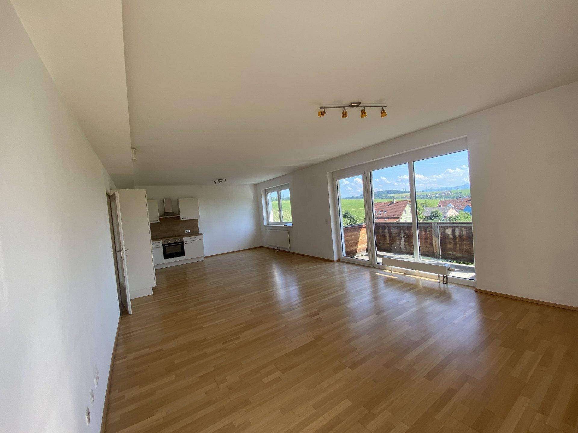 Geräumiger Wohnbereich mit Parkettboden, großen Fenstern und Zugang zum Balkon.