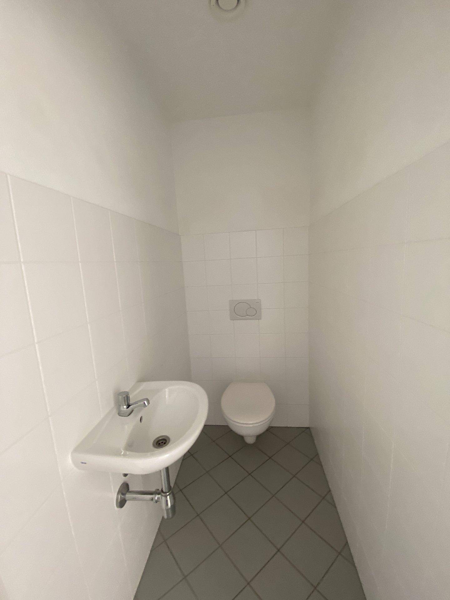 Helles Gäste-WC mit weißen Wandfliesen, grauen Bodenfliesen und modernem Waschbecken.