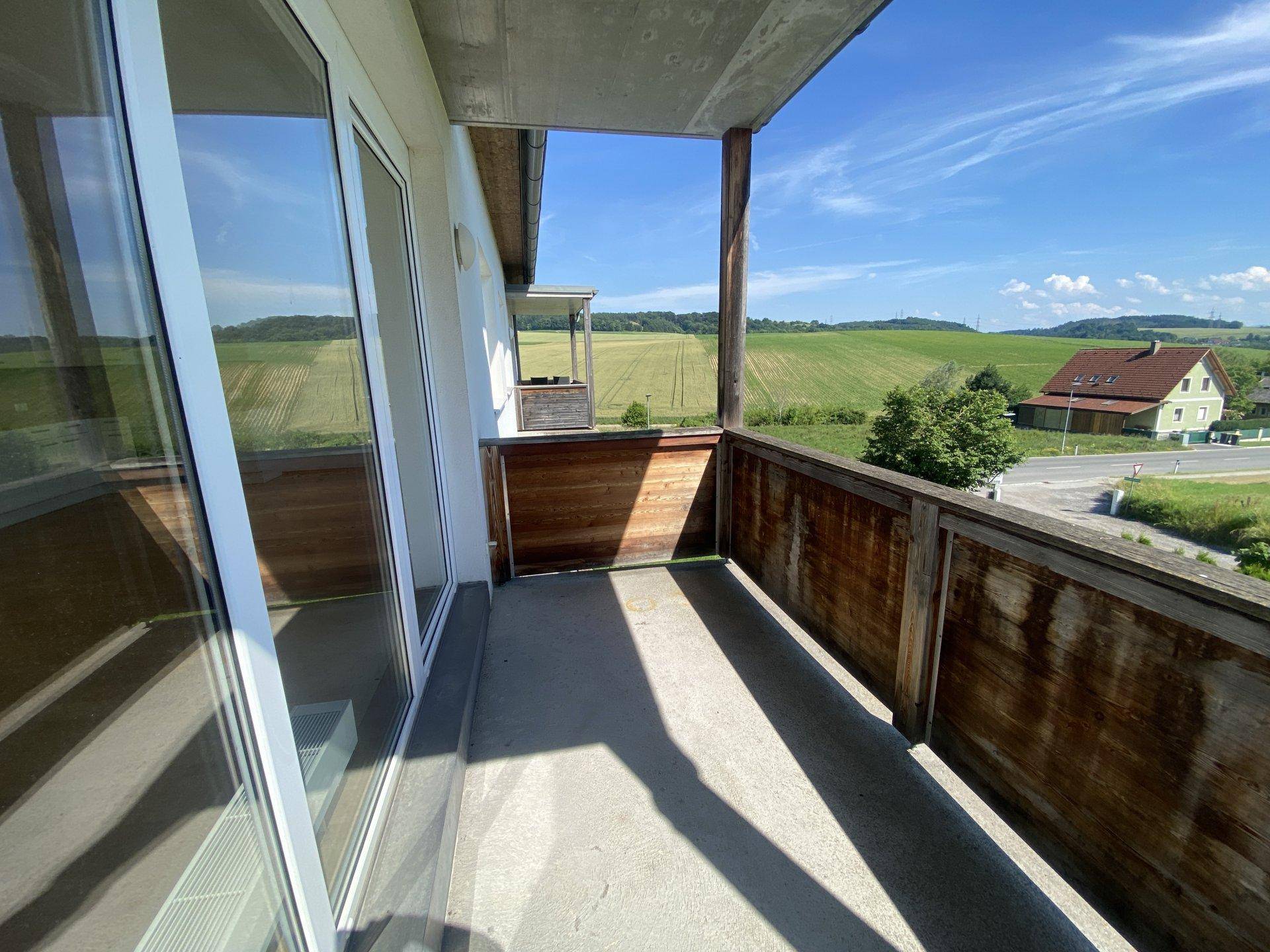 Geräumiger Balkon mit Holzelementen und weitem Blick über die grüne Landschaft.