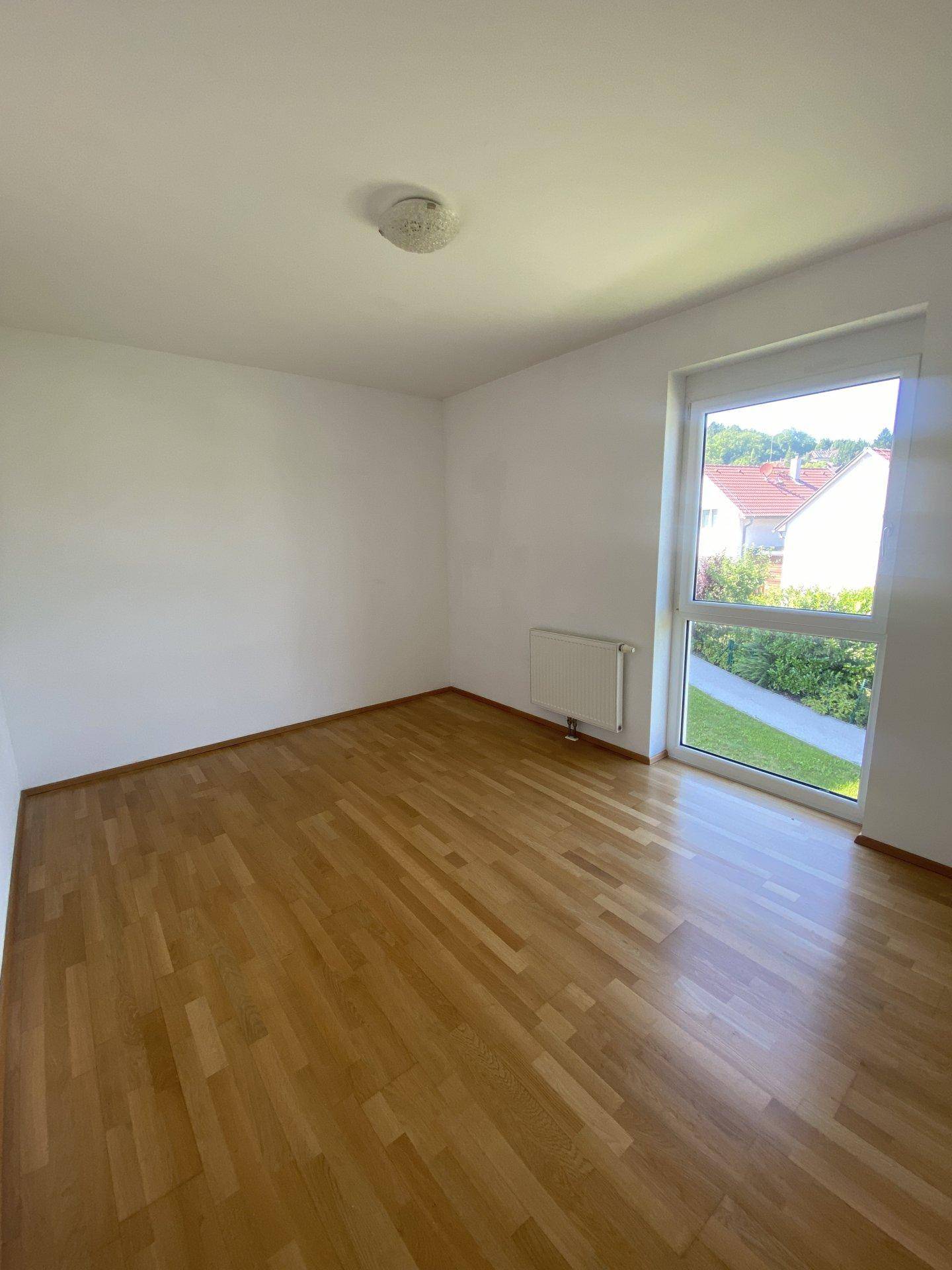 Lichtdurchflutetes Zimmer mit Parkettboden und Blick auf die grüne Umgebung.