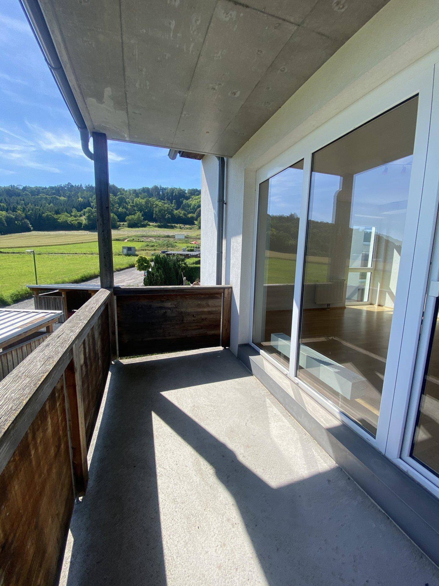 Balkon mit Betonboden und Holzgeländer, bietet einen schönen Blick ins Grüne.