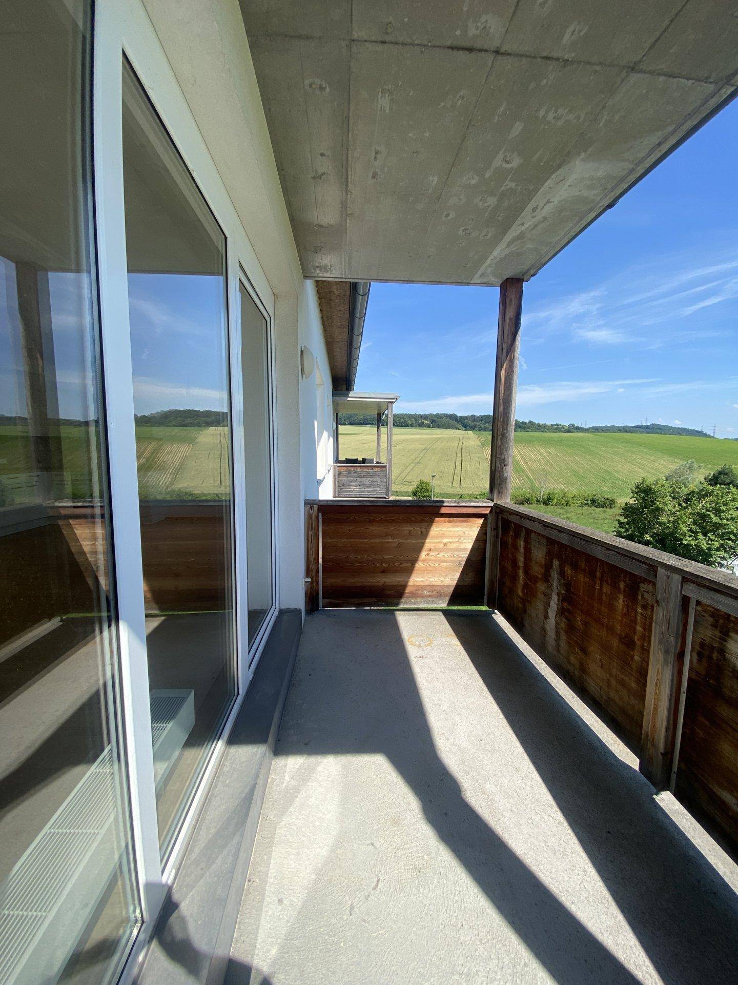 Sonniger Balkon mit Holzbalken und weitem Ausblick auf die umliegende Natur.