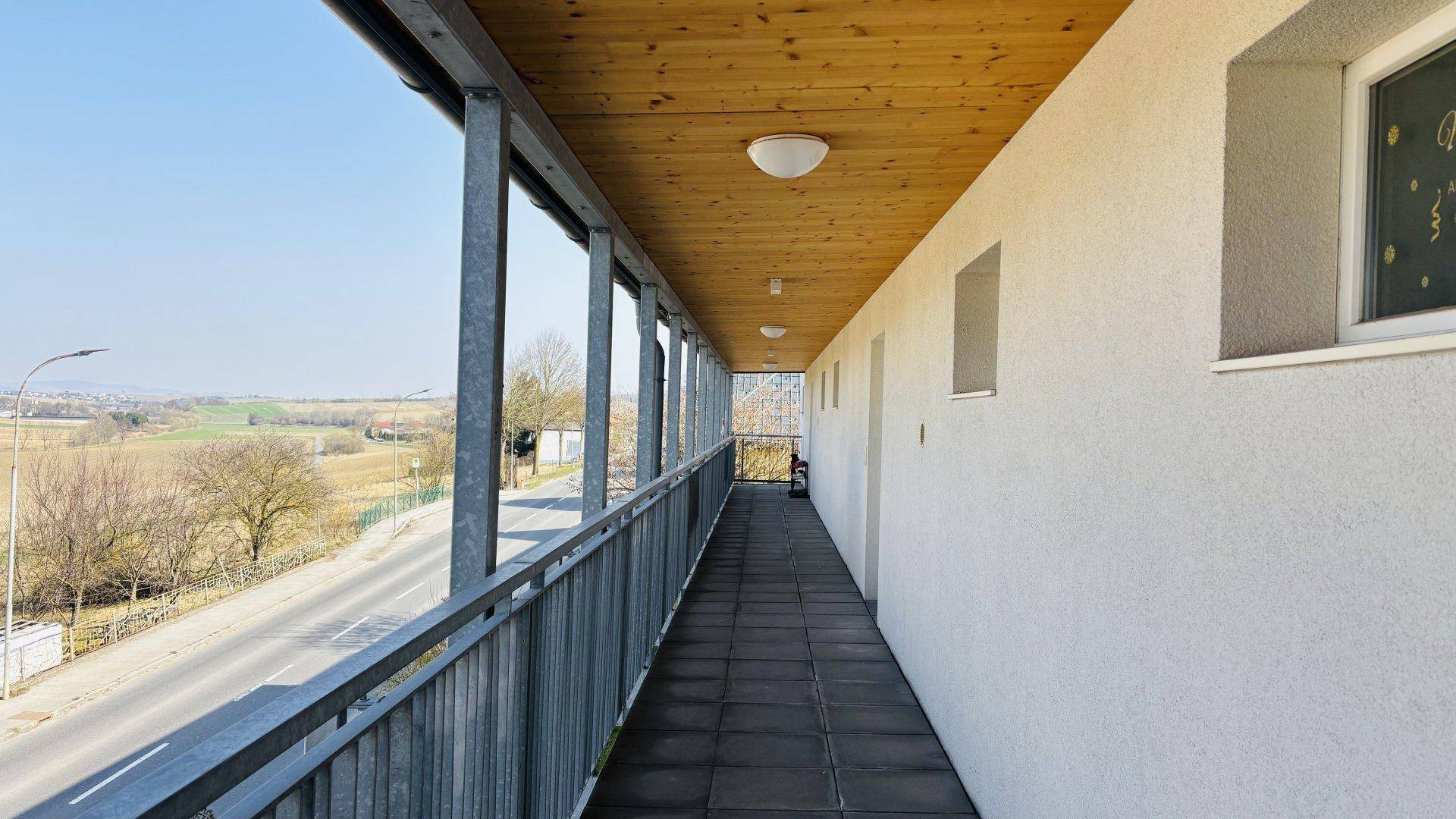 Lange überdachte Loggia mit Holzdecke und weitem Blick über die Landschaft und eine Straße.