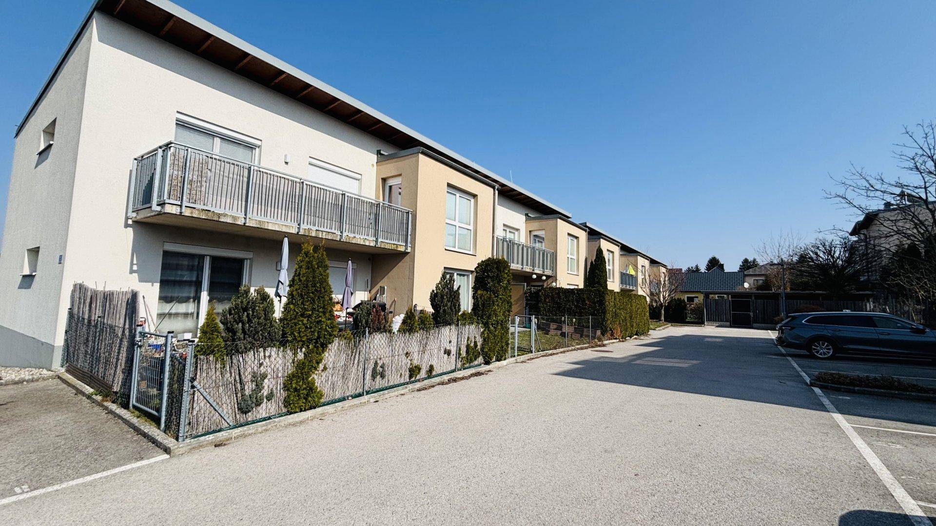 Reihenhausanlage mit Balkonen, kleinen Gärten und Parkplätzen im Freien.