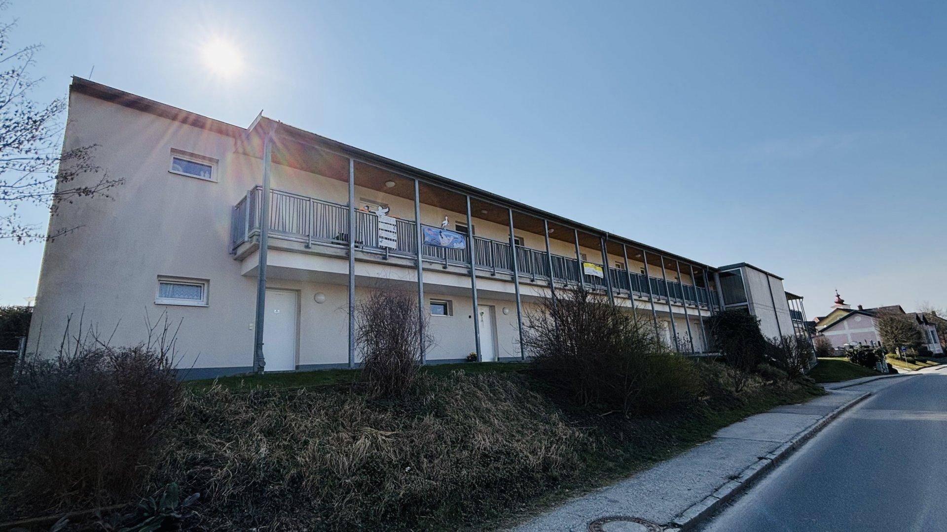 Lange Fassade eines modernen Wohngebäudes mit durchgehenden Balkonen unter strahlendem Himmel.
