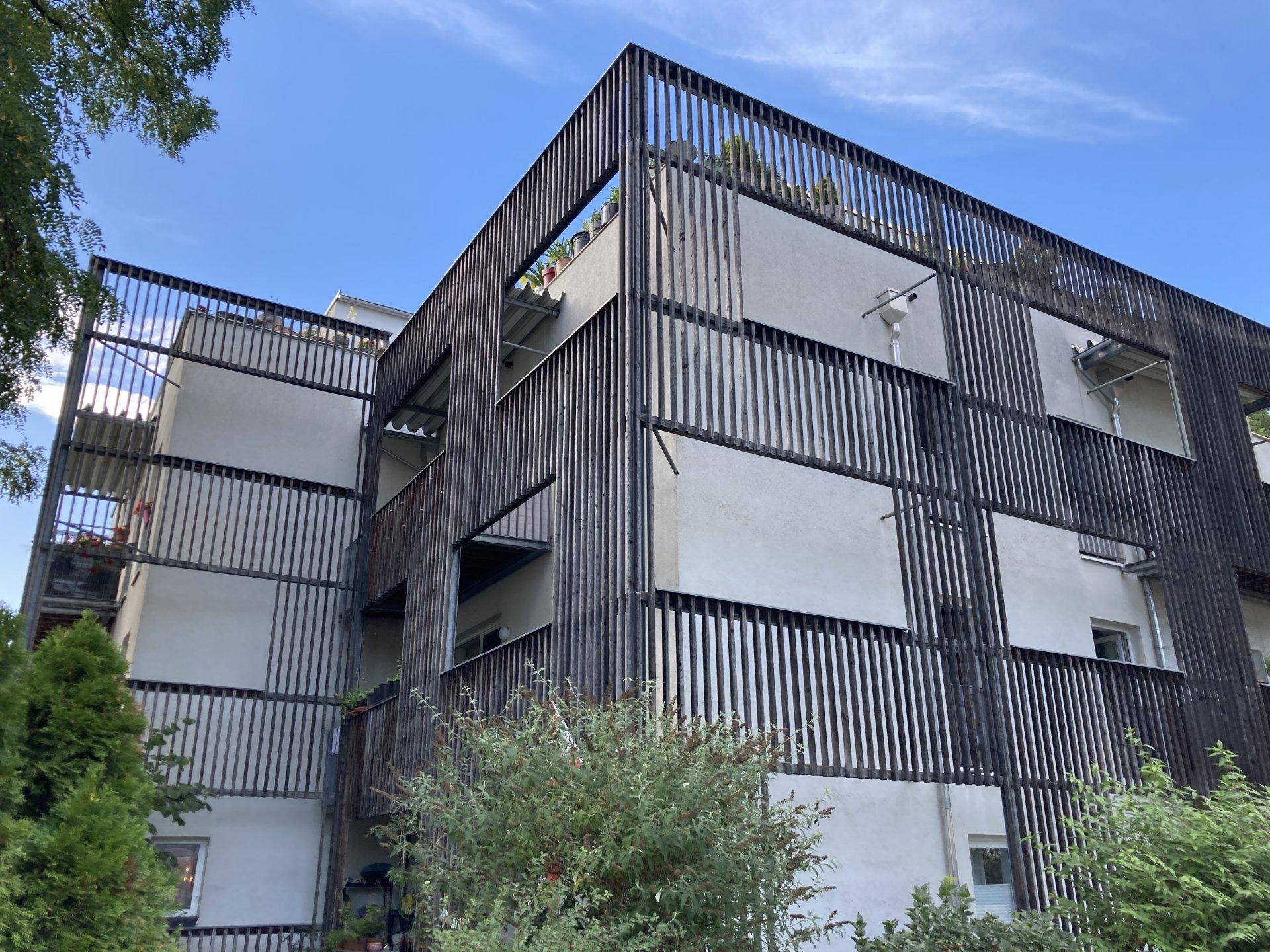 Architektonisch ansprechendes Gebäude mit dunklen Holzlamellen an der Fassade und mehreren Balkonen.